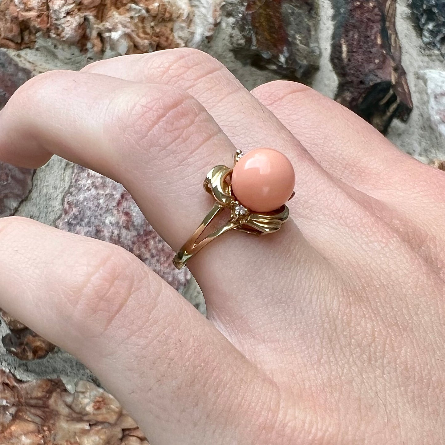 A vintage split shank flower ring set with a round pink coral sphere and diamond accents.