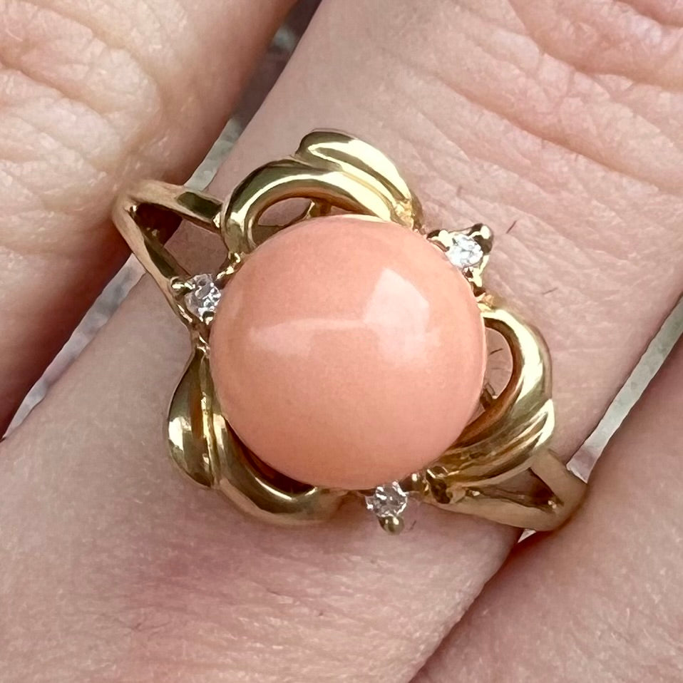 A vintage split shank flower ring set with a round pink coral sphere and diamond accents.