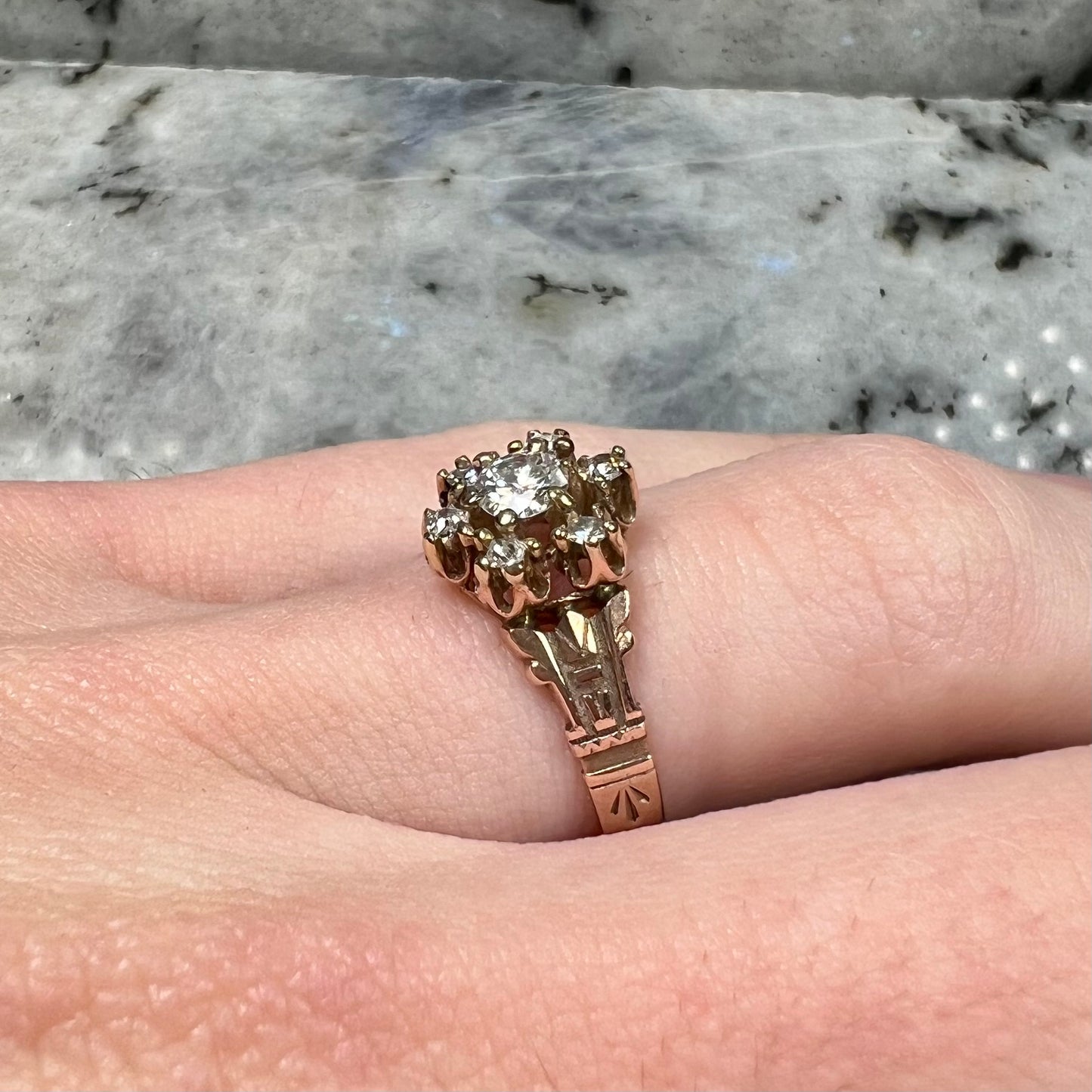 A modern Standard Round Brilliant Cut diamond set between six smaller round diamonds in an antique rose gold engagement ring setting.