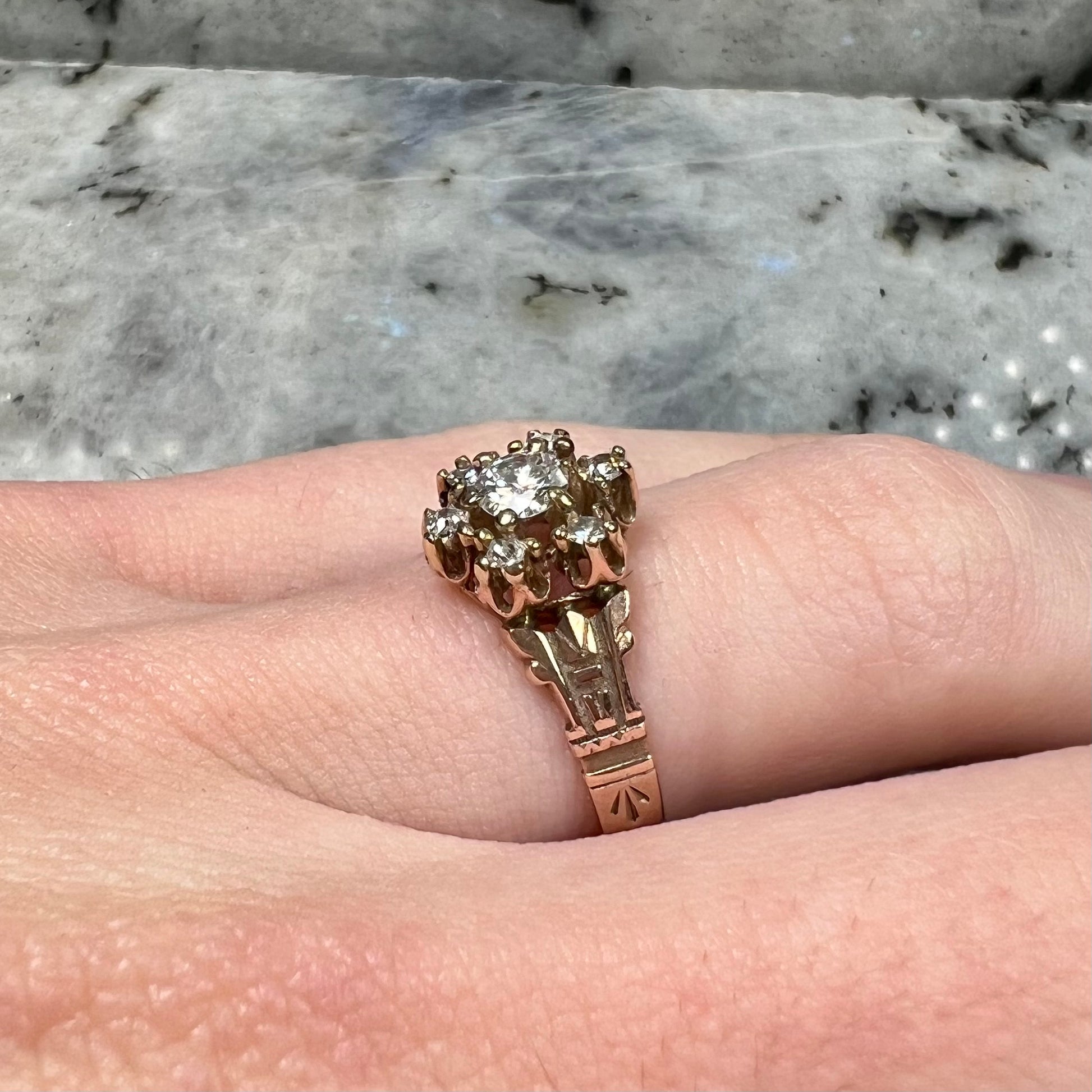 A modern Standard Round Brilliant Cut diamond set between six smaller round diamonds in an antique rose gold engagement ring setting.