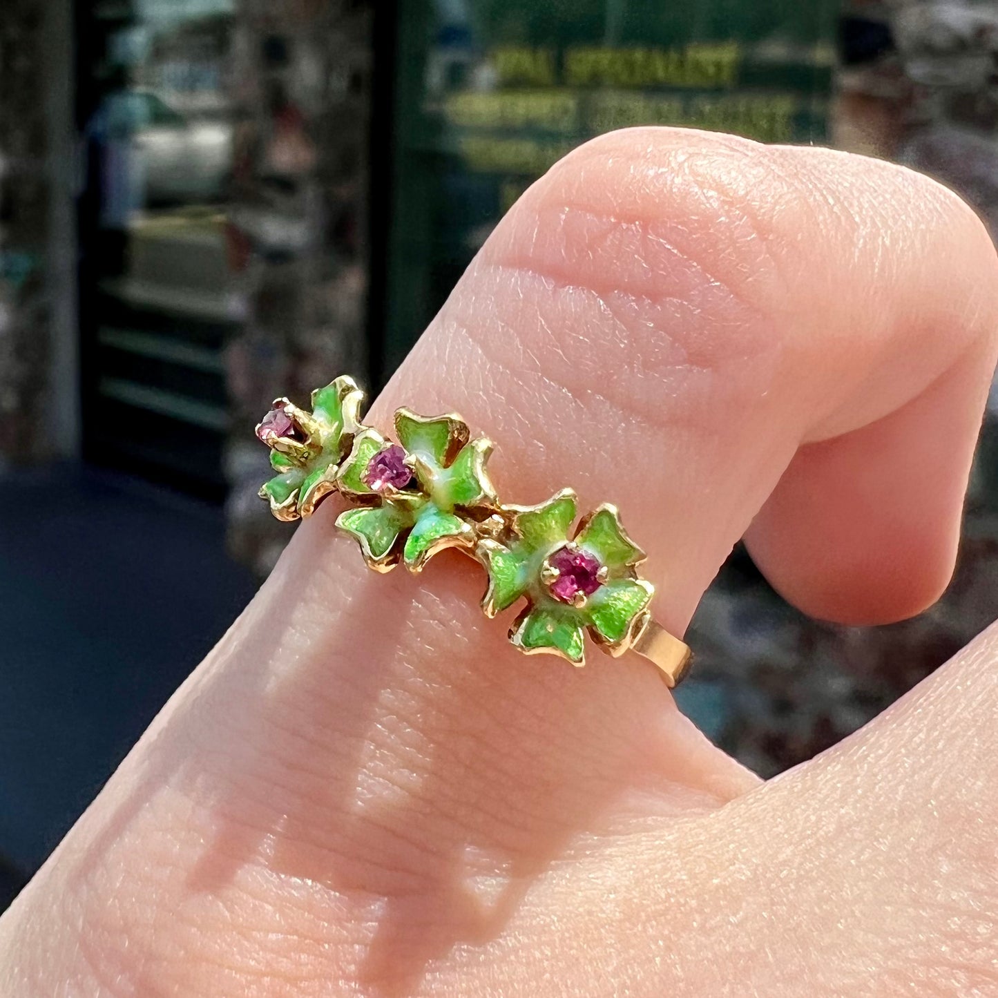 A gold ladies' ring in the motif of three flowers set with round ruby centers and green enameled petals.