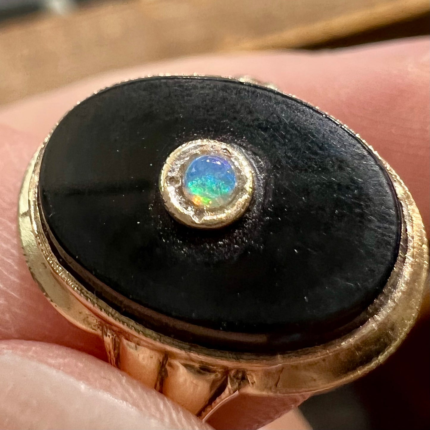 A yellow gold onyx ring set with a round cabochon cut opal bezel set into the onyx.