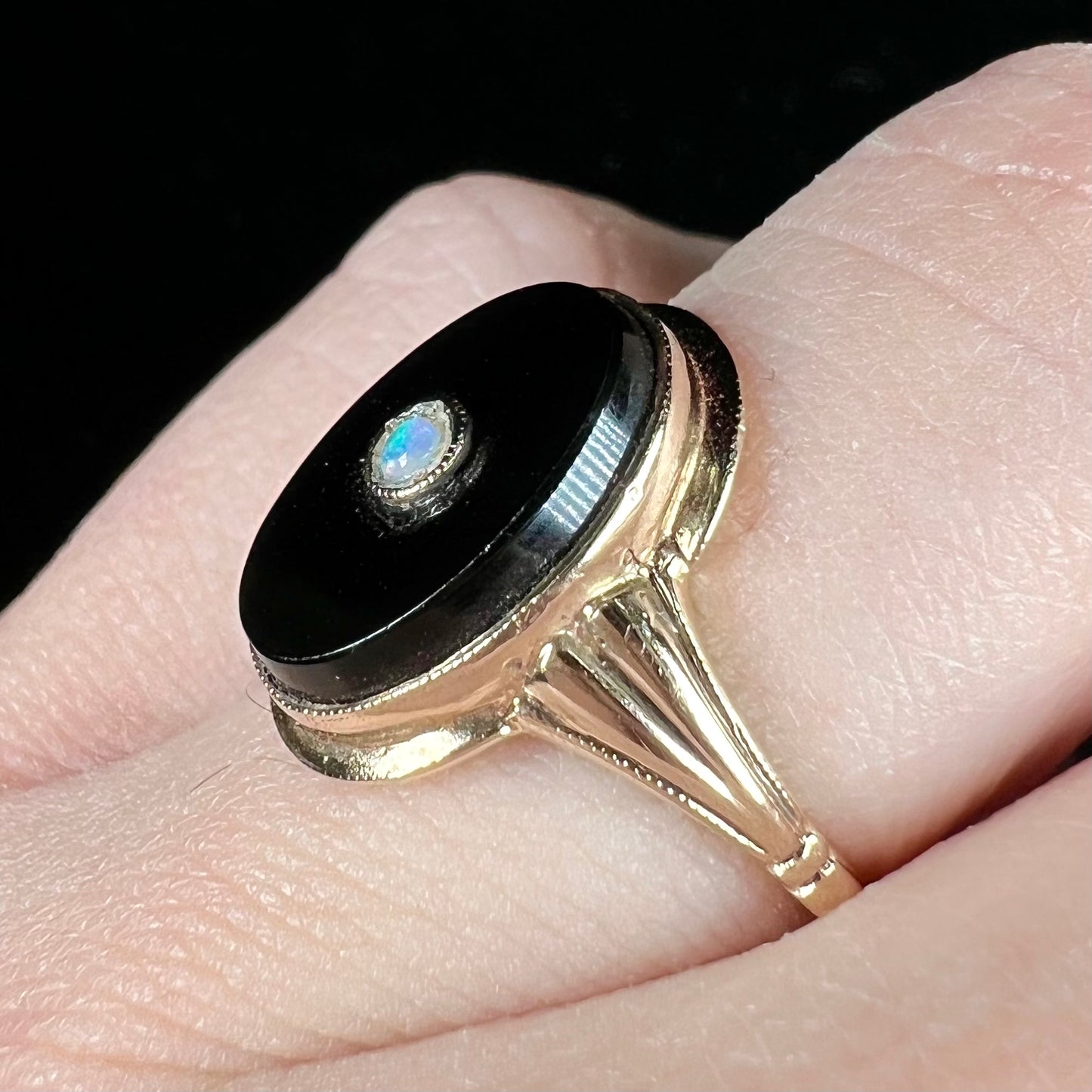 A yellow gold onyx ring set with a round cabochon cut opal bezel set into the onyx.