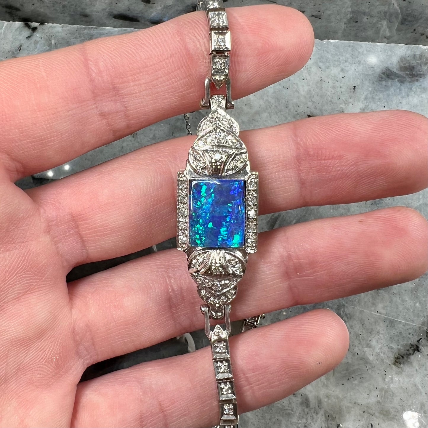 A vintage, art deco style white gold and diamond bracelet set with a rectangular shape black boulder opal stone.