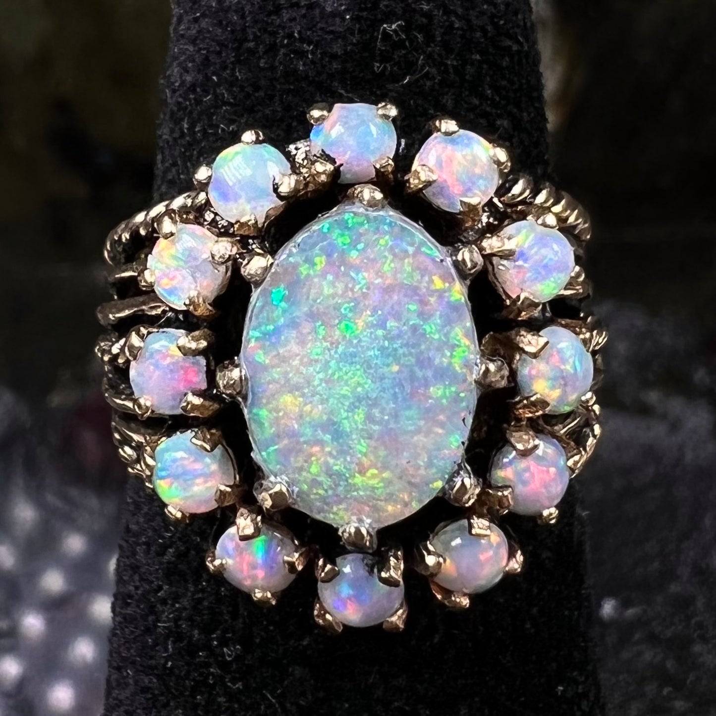 Vintage yellow gold oval opal cabochon ring set with 12 round opals in a halo around the center stone.