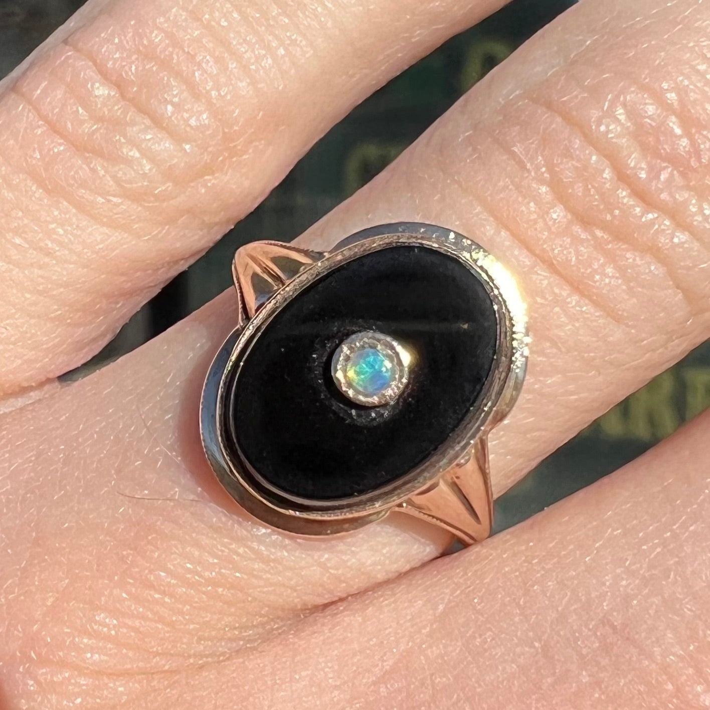 A yellow gold onyx ring set with a round cabochon cut opal bezel set into the onyx.