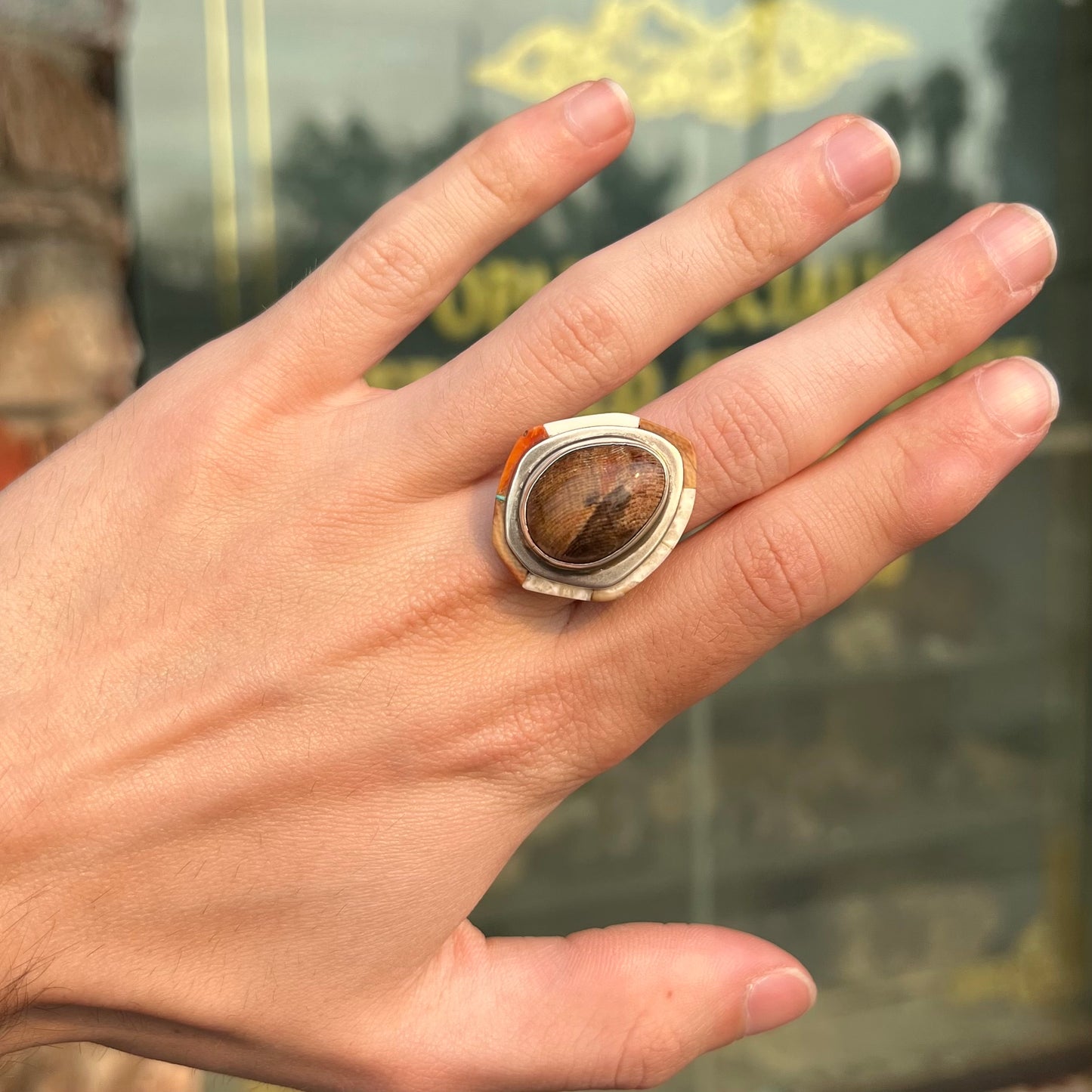 A silver ring handmade from a bezel set petrified wood stone, surrounded by quartz, carnelian, and bone inlay.