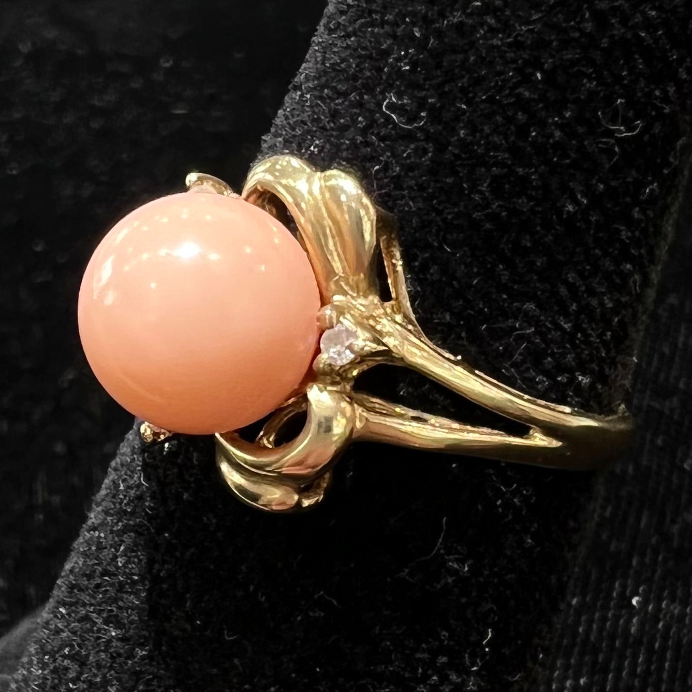 A vintage split shank flower ring set with a round pink coral sphere and diamond accents.