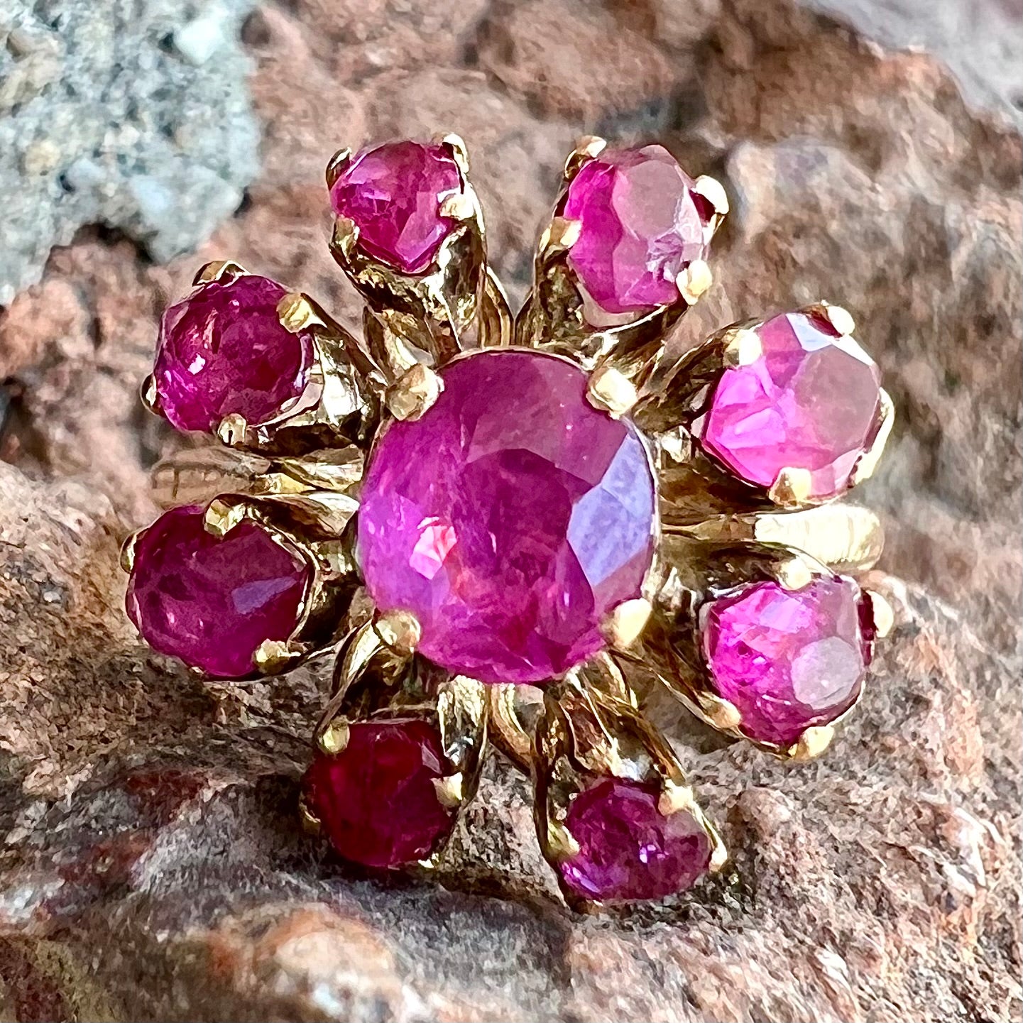 A yellow gold pink Burma ruby cluster ring with a faceted oval center stone surrounded by marquise cut stones.