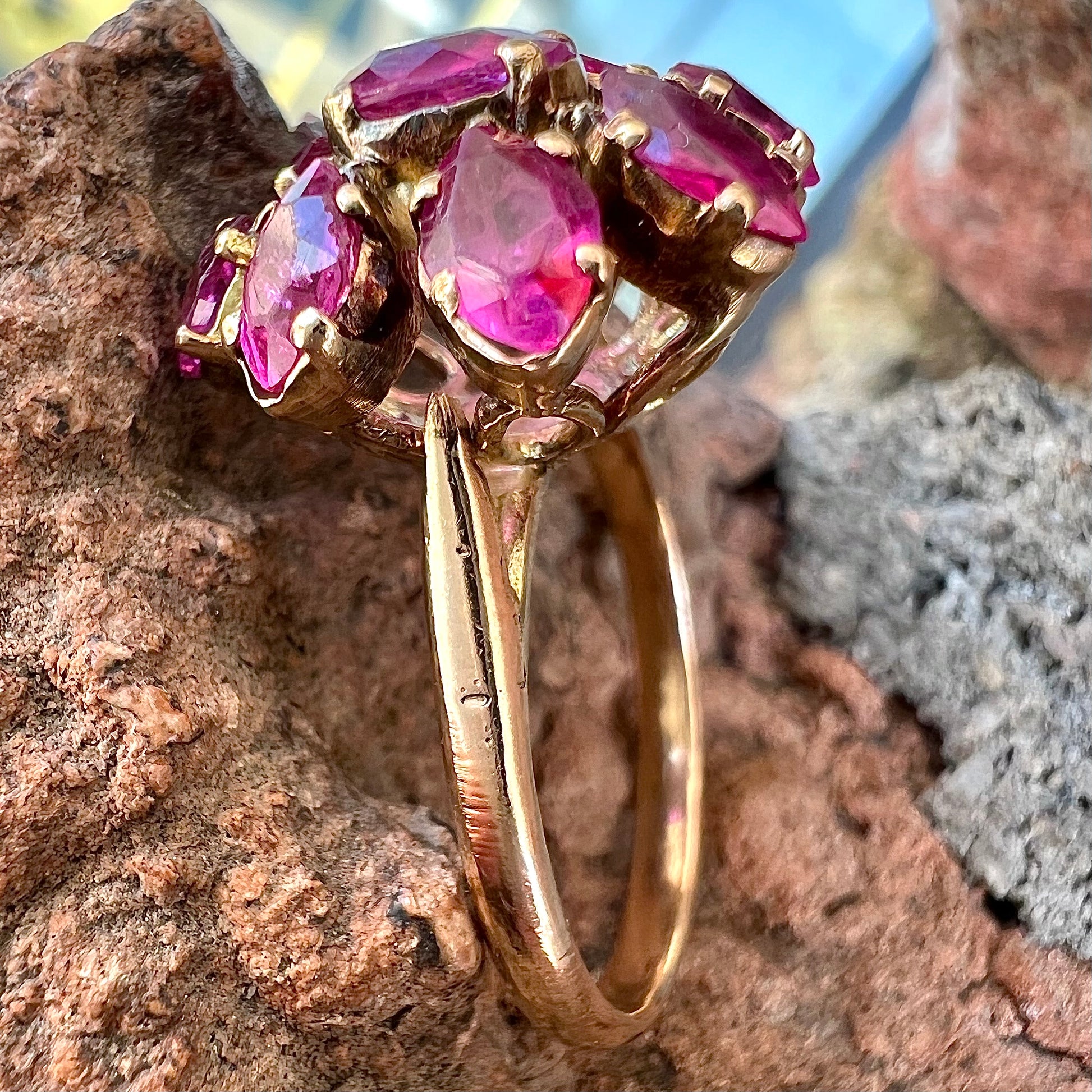 A yellow gold pink Burma ruby cluster ring with a faceted oval center stone surrounded by marquise cut stones.