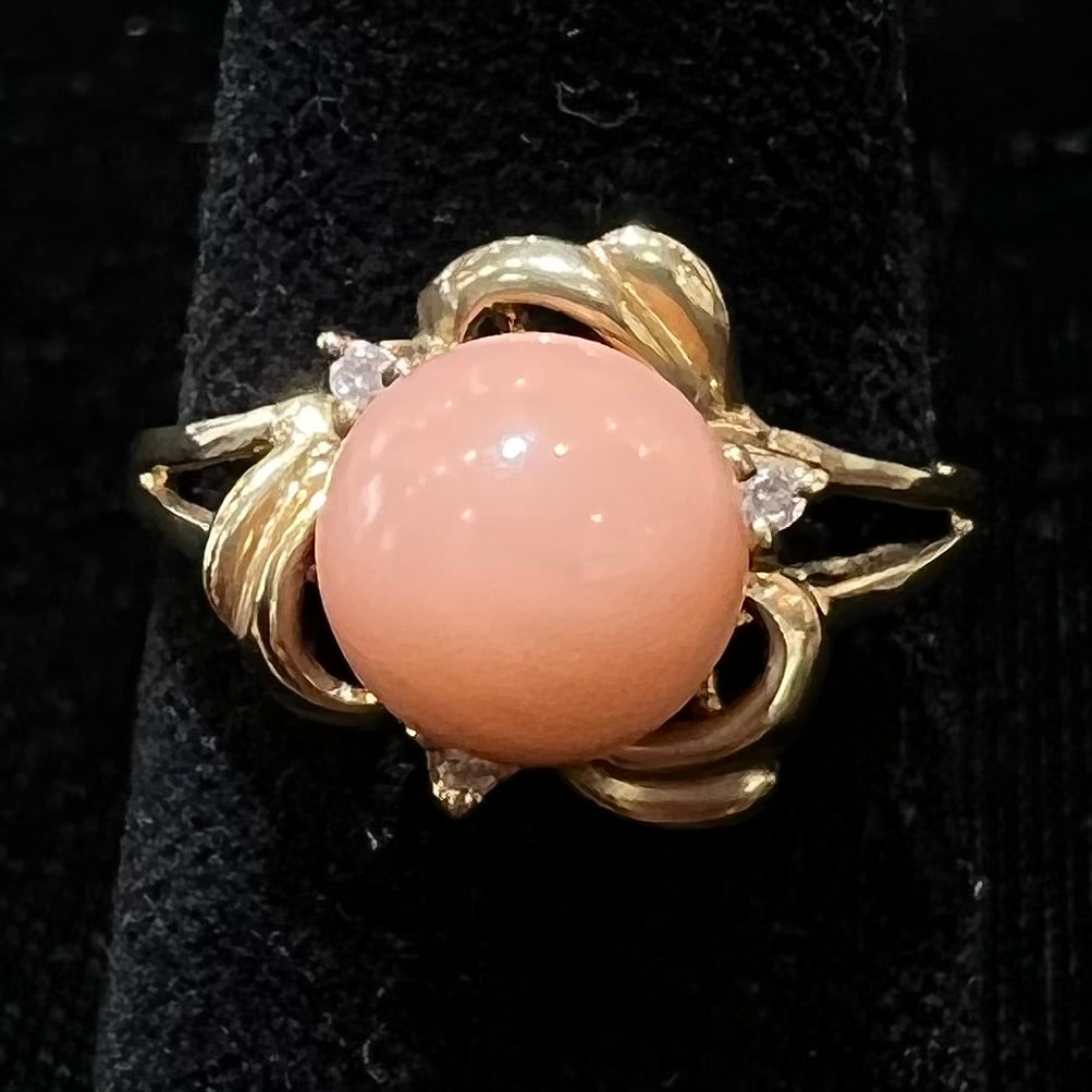 A vintage split shank flower ring set with a round pink coral sphere and diamond accents.
