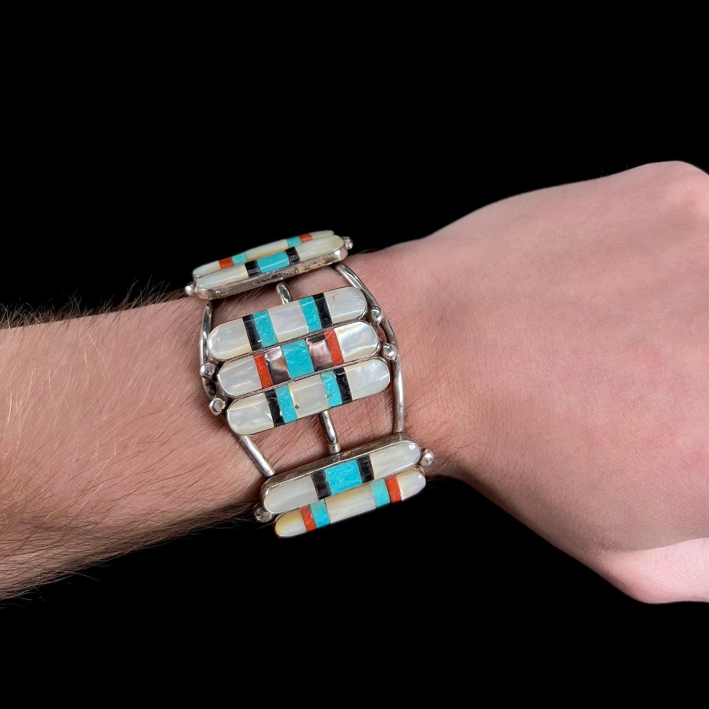 A vintage Zuni Indian-made inlay cuff bracelet set with mother of pearl, coral, turquoise, and jet stones. The piece is signed "PONCHO."