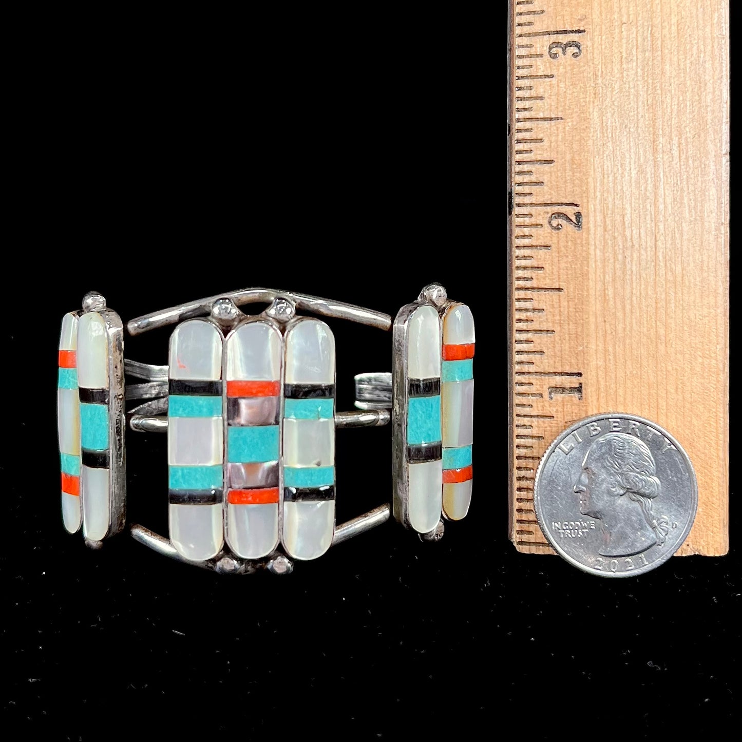 A vintage Zuni Indian-made inlay cuff bracelet set with mother of pearl, coral, turquoise, and jet stones. The piece is signed "PONCHO."