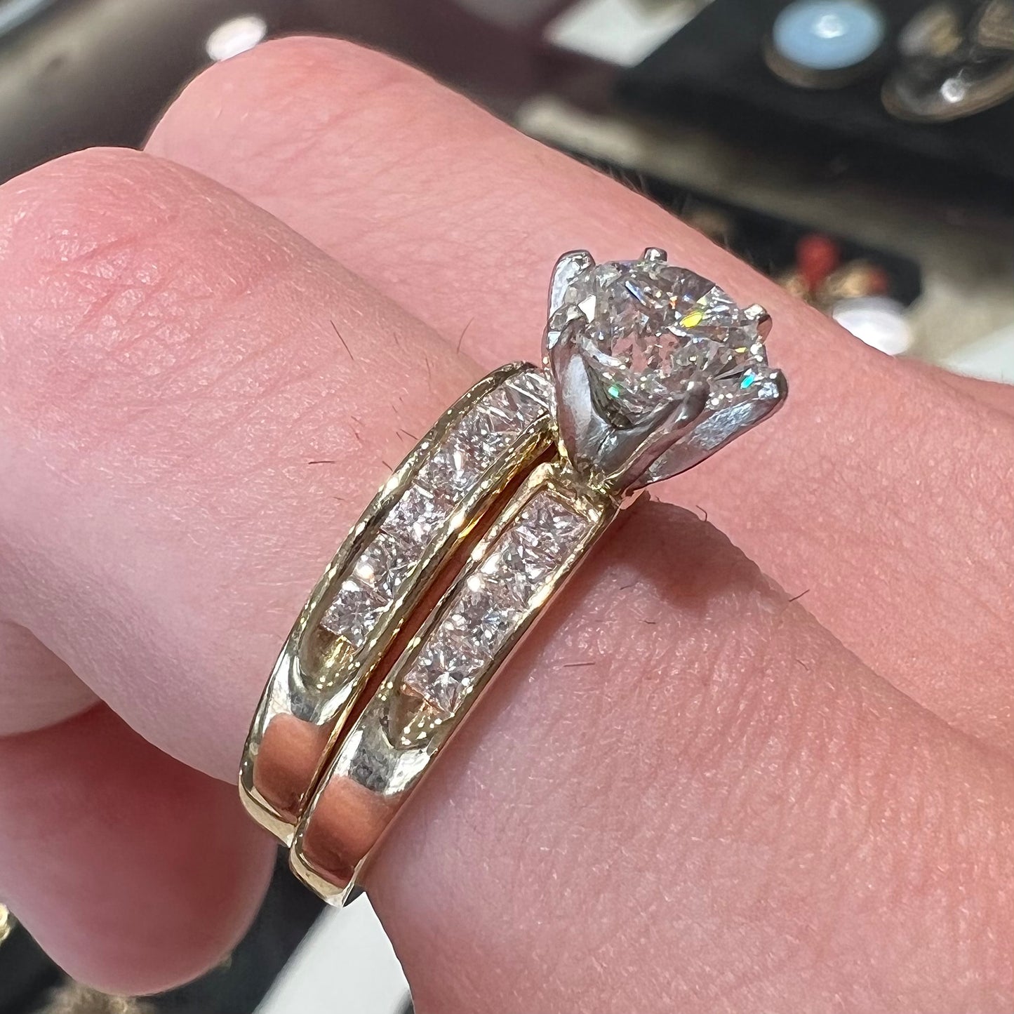 A diamond engagement and wedding ring set. The center stone is a 1 carat round diamond, and the side stones are channel set princess cut diamonds.