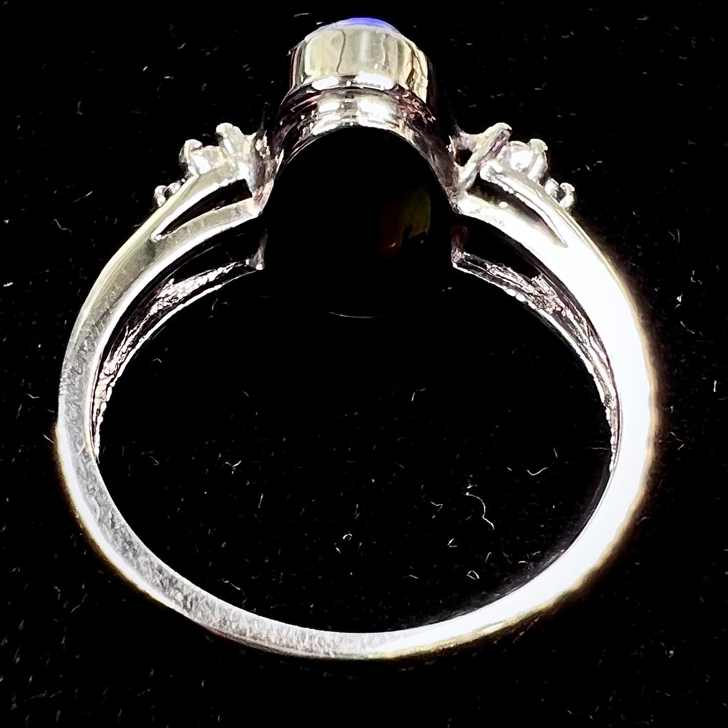 A white gold ring set with a Lightning Ridge black opal and diamond accents. The opal displays a cat's eye pattern.