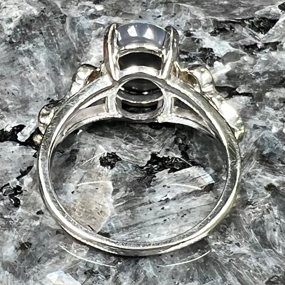 A white gold, oval cabochon cut black opal doublet ring set with two round diamond accent stones.