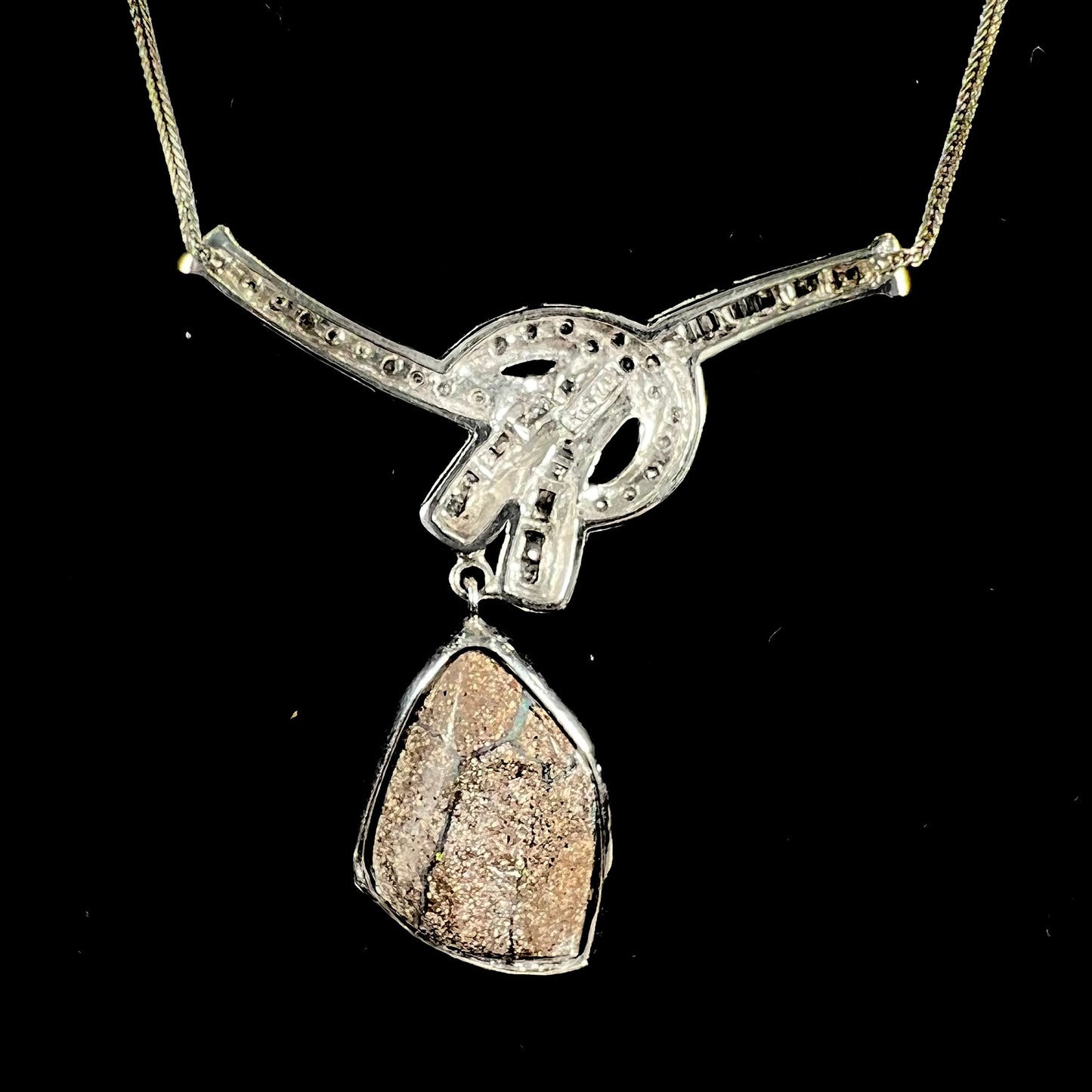 A white gold necklace set with diamonds and a dangling, bezel set boulder opal.