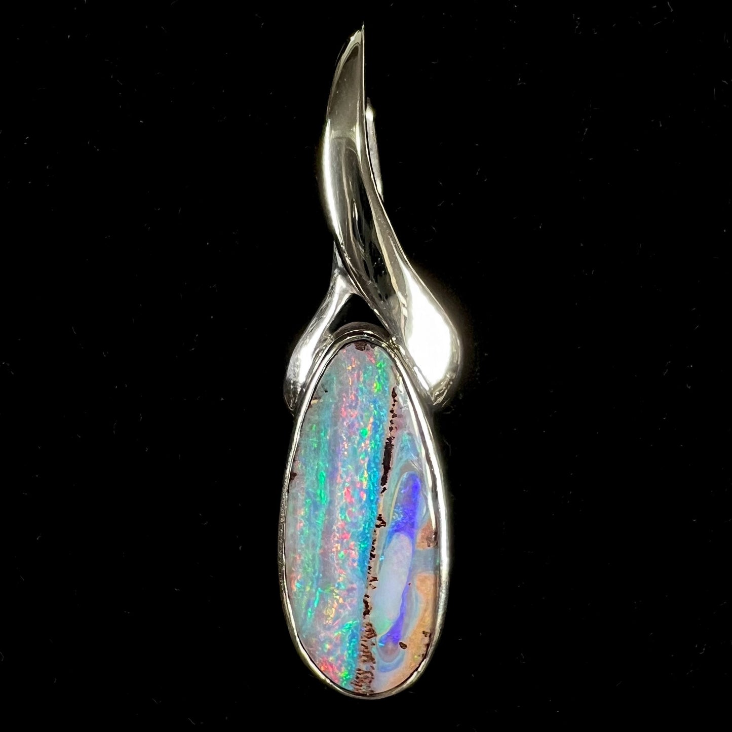 A white gold solitaire pendant set with an Quilpie, Australian boulder opal stone. The opal shines a rainbow of colors.