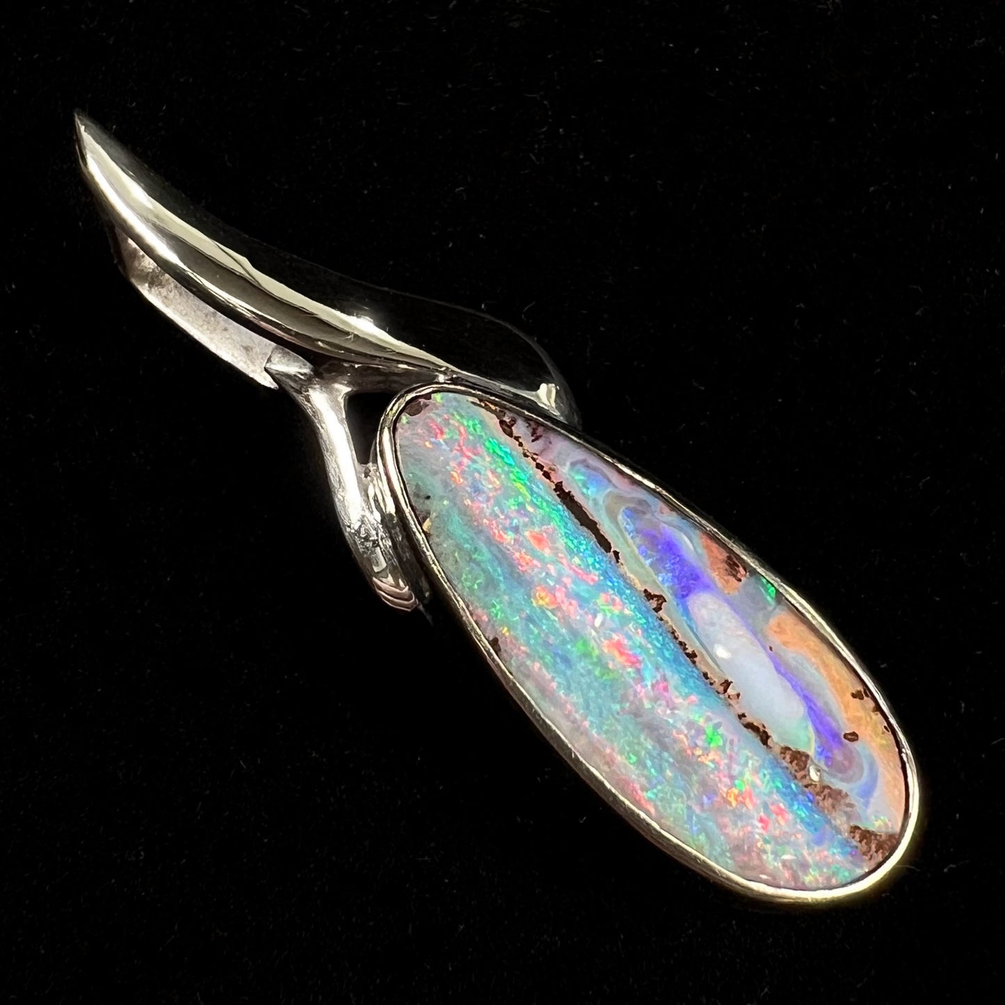 A white gold solitaire pendant set with an Quilpie, Australian boulder opal stone. The opal shines a rainbow of colors.
