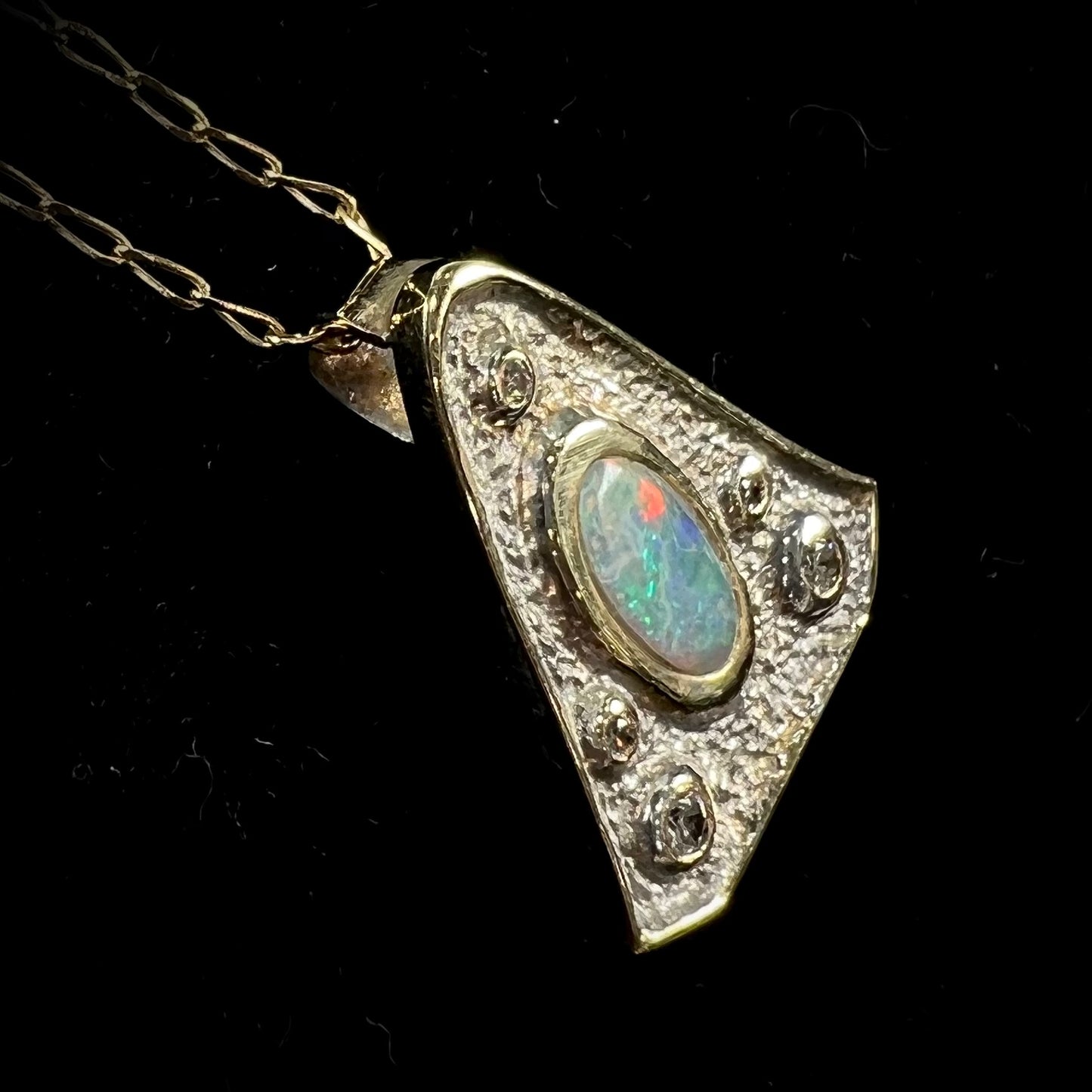A triangular gold pendant set with five round diamonds and a white crystal opal with green fire.