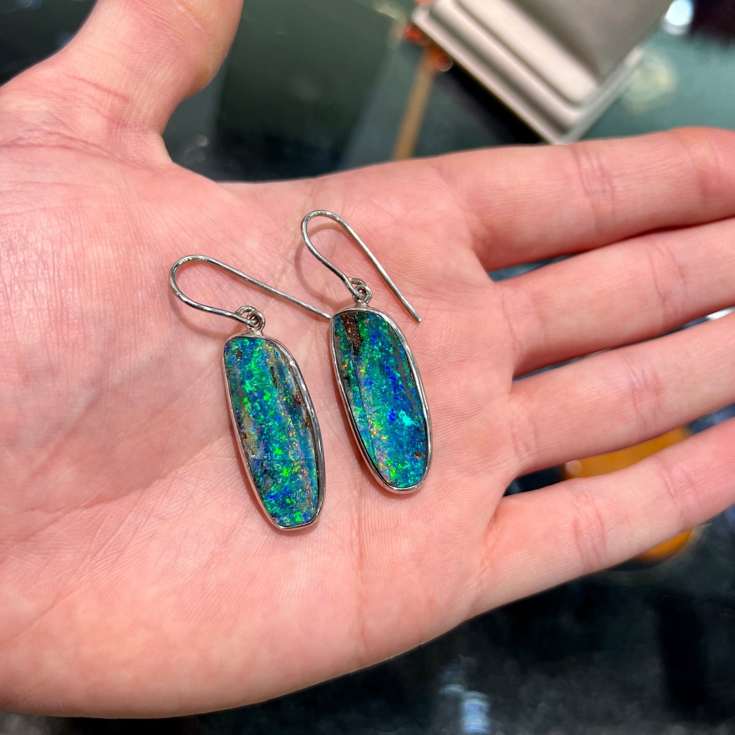 A pair of white gold boulder opal French wire dangle earrings. The opal is predominantly glimmery blue.