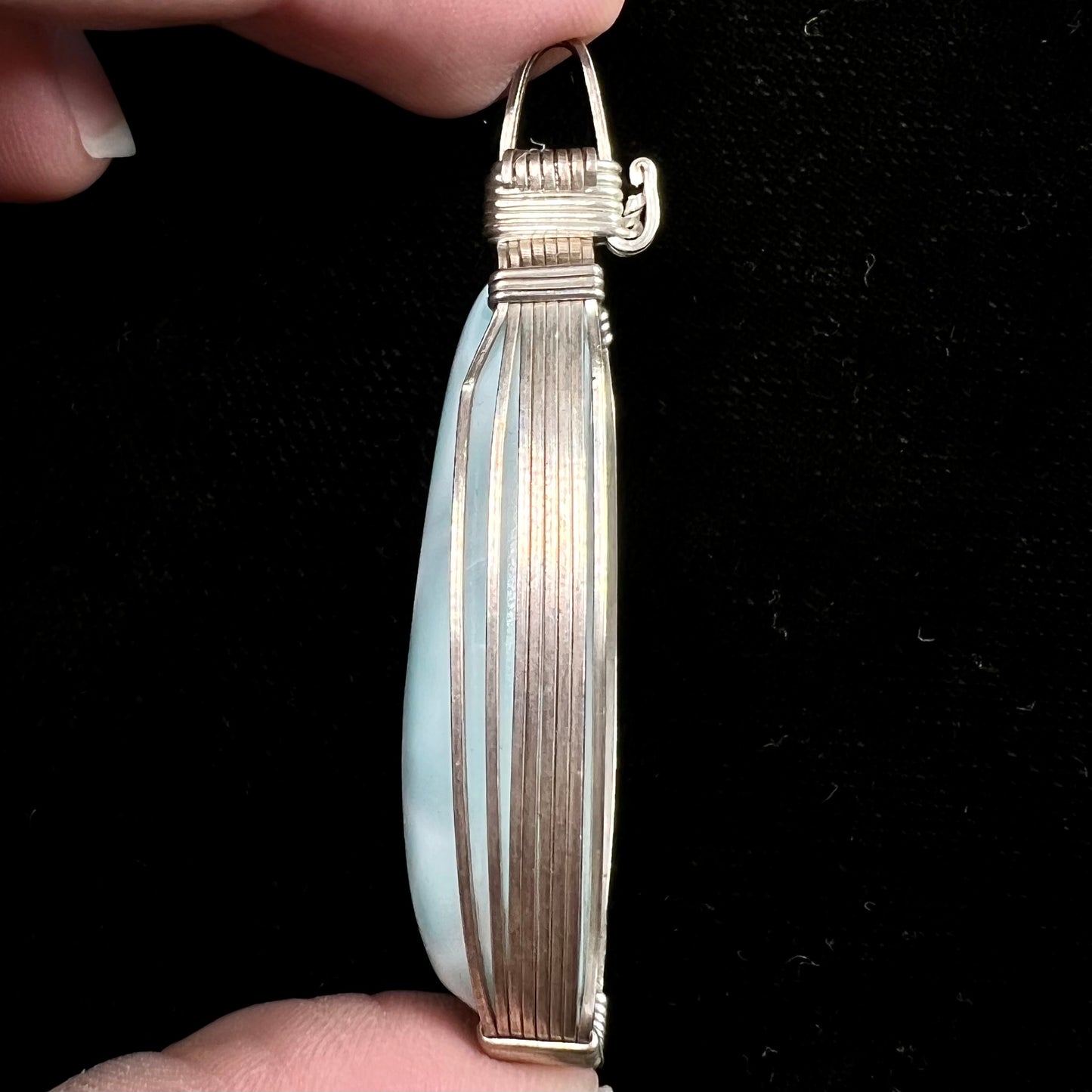 A large, oval cabochon cut blue larimar stone mounted in a sterling silver wire wrapped pendant.