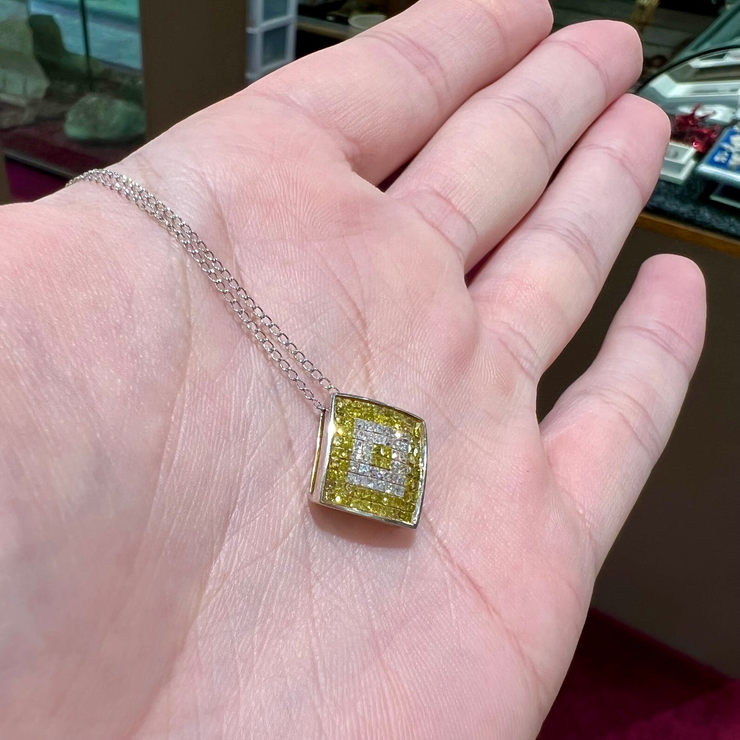 A square shaped necklace set with princess cut yellow and white diamonds in a white gold setting on a white gold chain.