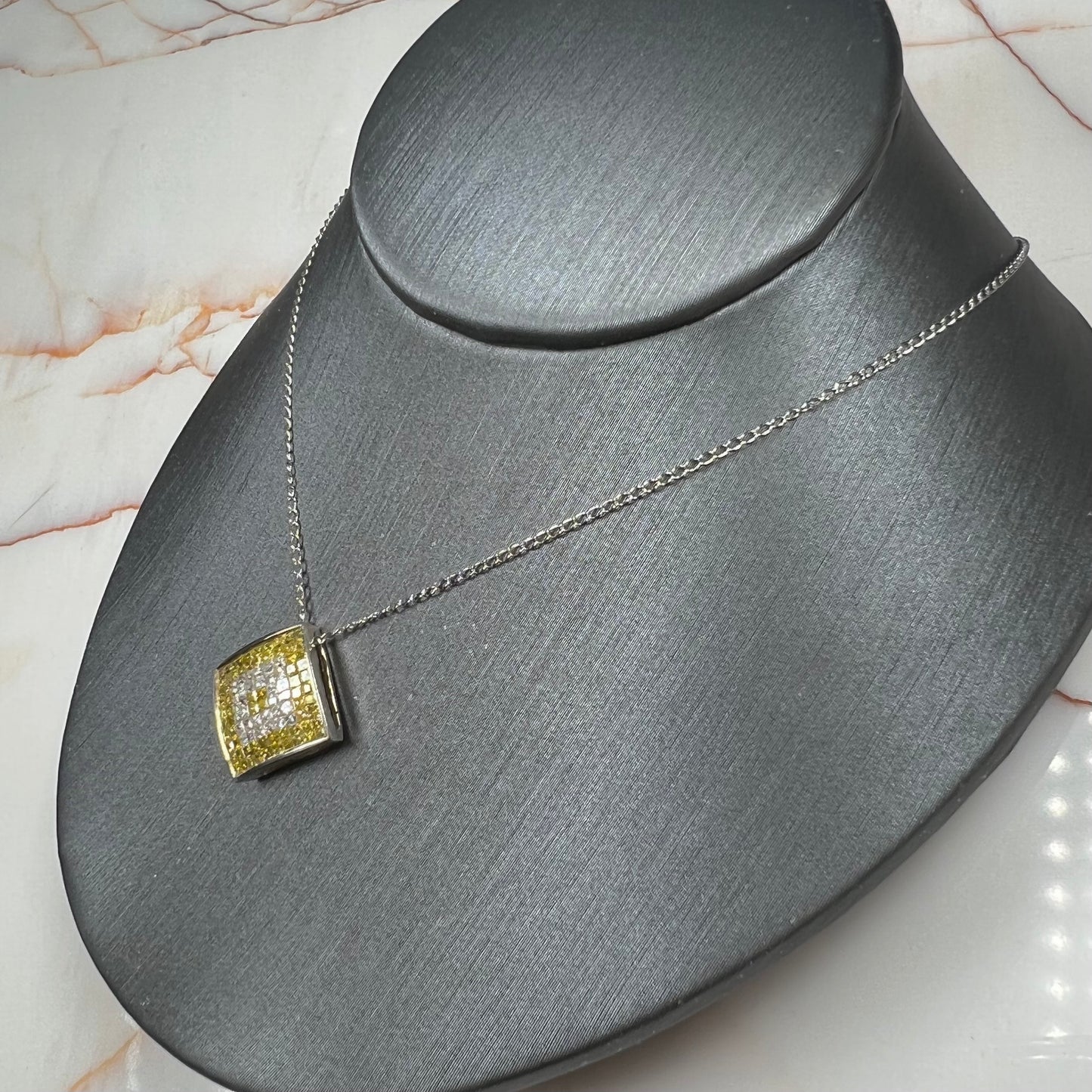 A square shaped necklace set with princess cut yellow and white diamonds in a white gold setting on a white gold chain.