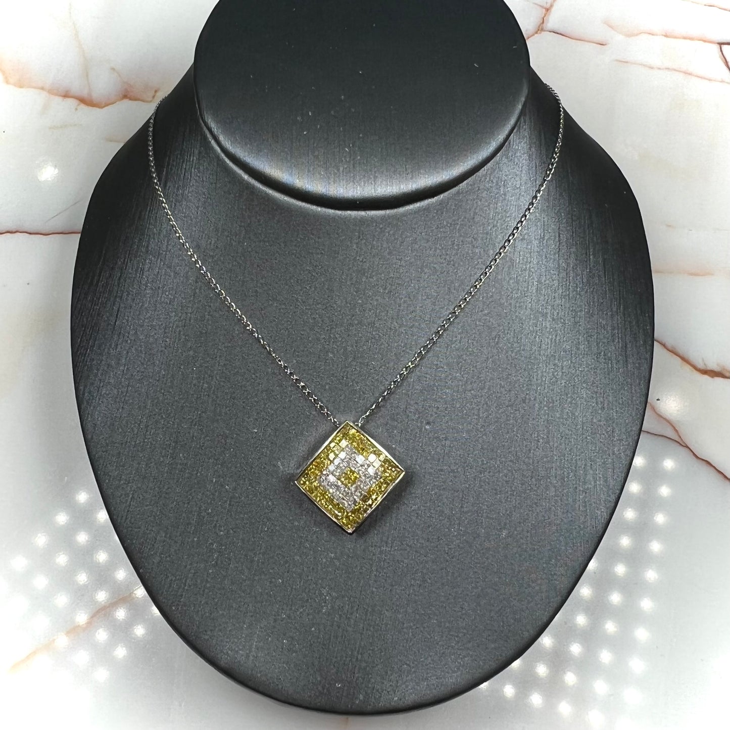 A square shaped necklace set with princess cut yellow and white diamonds in a white gold setting on a white gold chain.