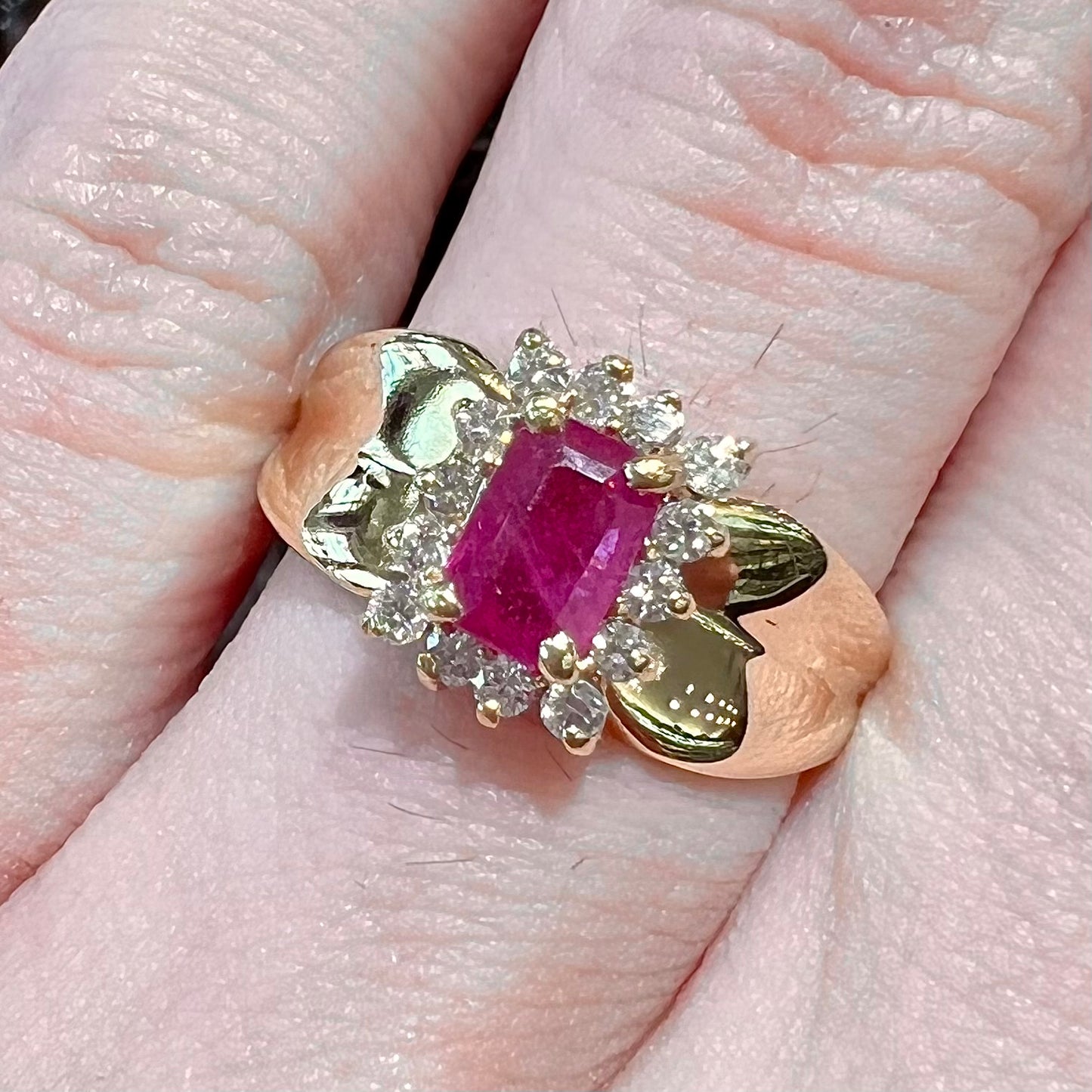 A yellow gold ring set with an emerald cut red ruby surrounded by a halo of round diamonds.