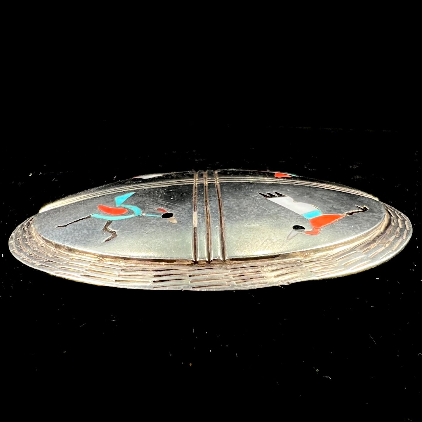 A silver pendant of two flying cranes and two roadrunners inlaid with turquoise, coral, and mother of pearl.