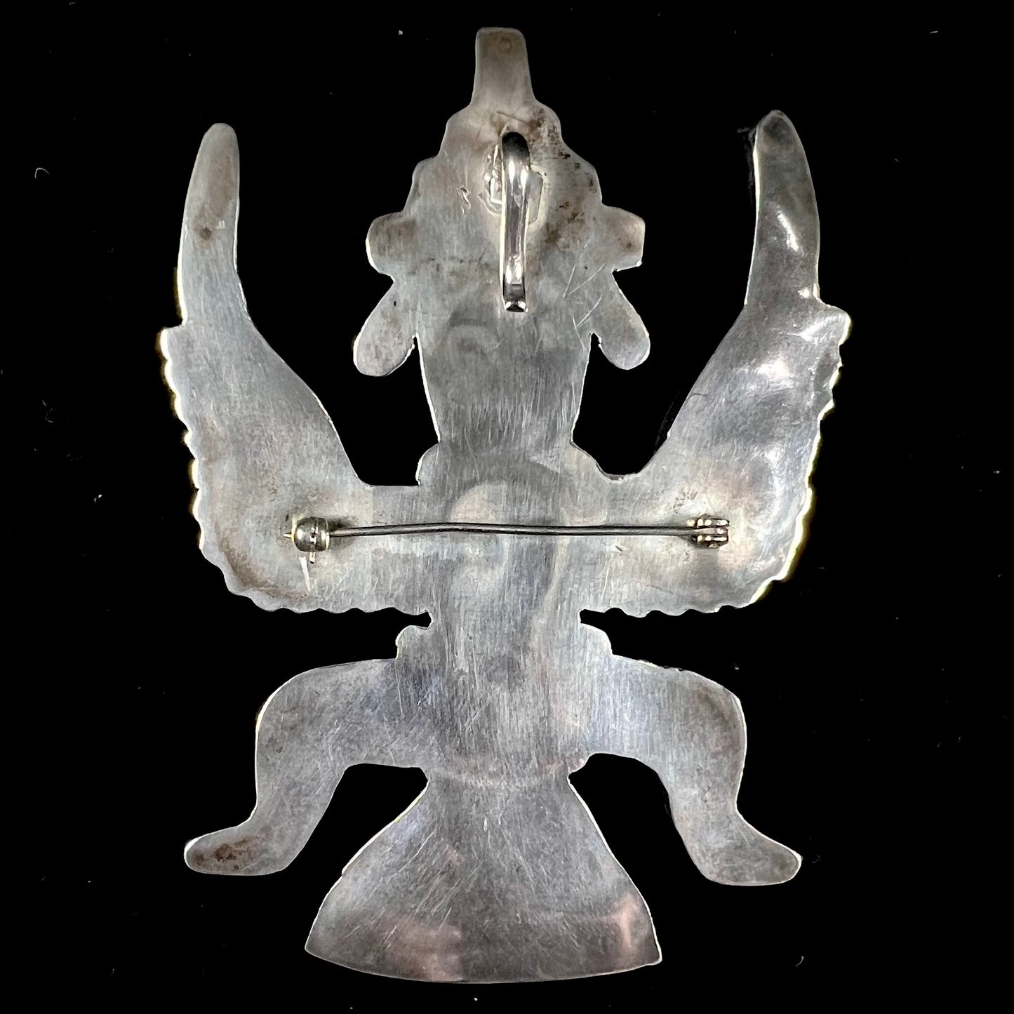 A silver, Zuni Indian dancing eagle necklace/pin. The piece is inlaid with pieces of onyx, turquoise, coral, and mother of pearl.