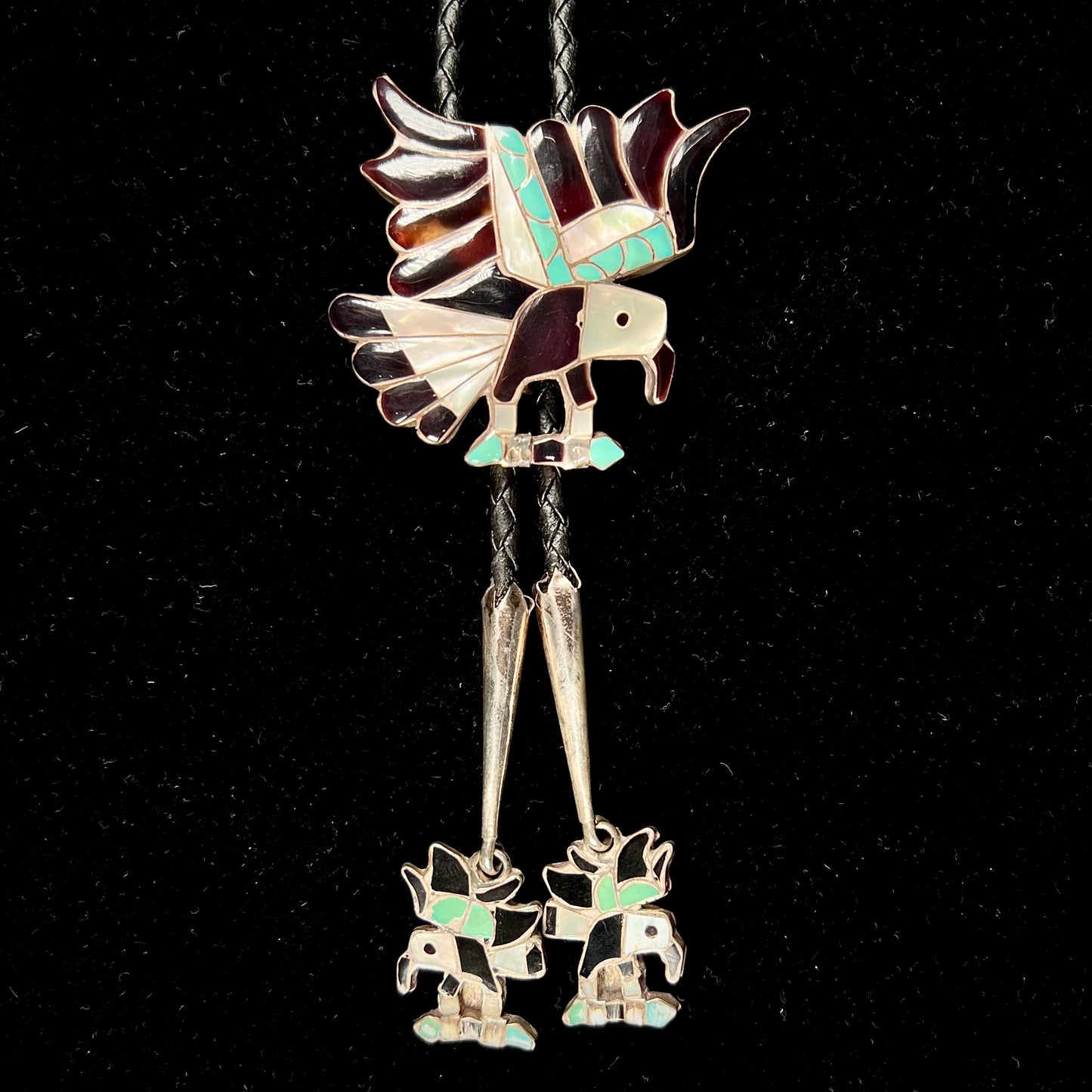 A sterling silver Zuni Indian-made bolo tie featuring the motif of three flying eagles inlaid with natural stones.
