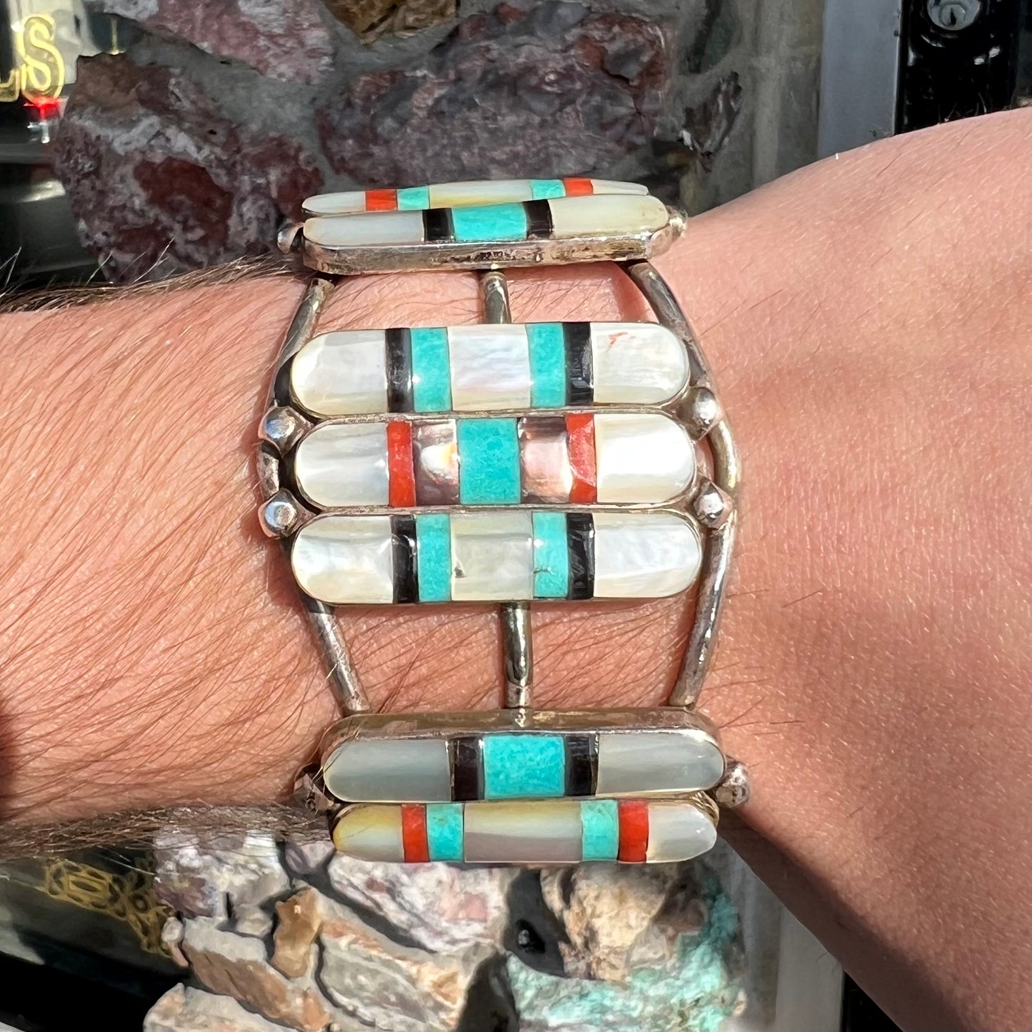 A vintage Zuni Indian-made inlay cuff bracelet set with mother of pearl, coral, turquoise, and jet stones. The piece is signed "PONCHO."