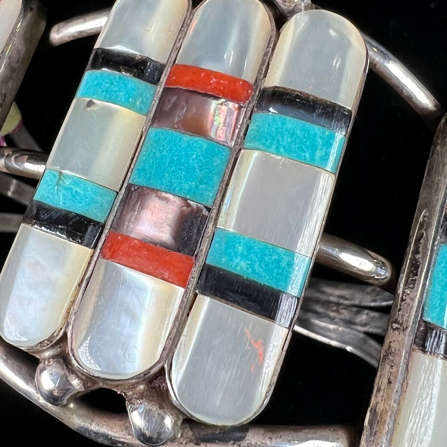 A vintage Zuni Indian-made inlay cuff bracelet set with mother of pearl, coral, turquoise, and jet stones. The piece is signed "PONCHO."