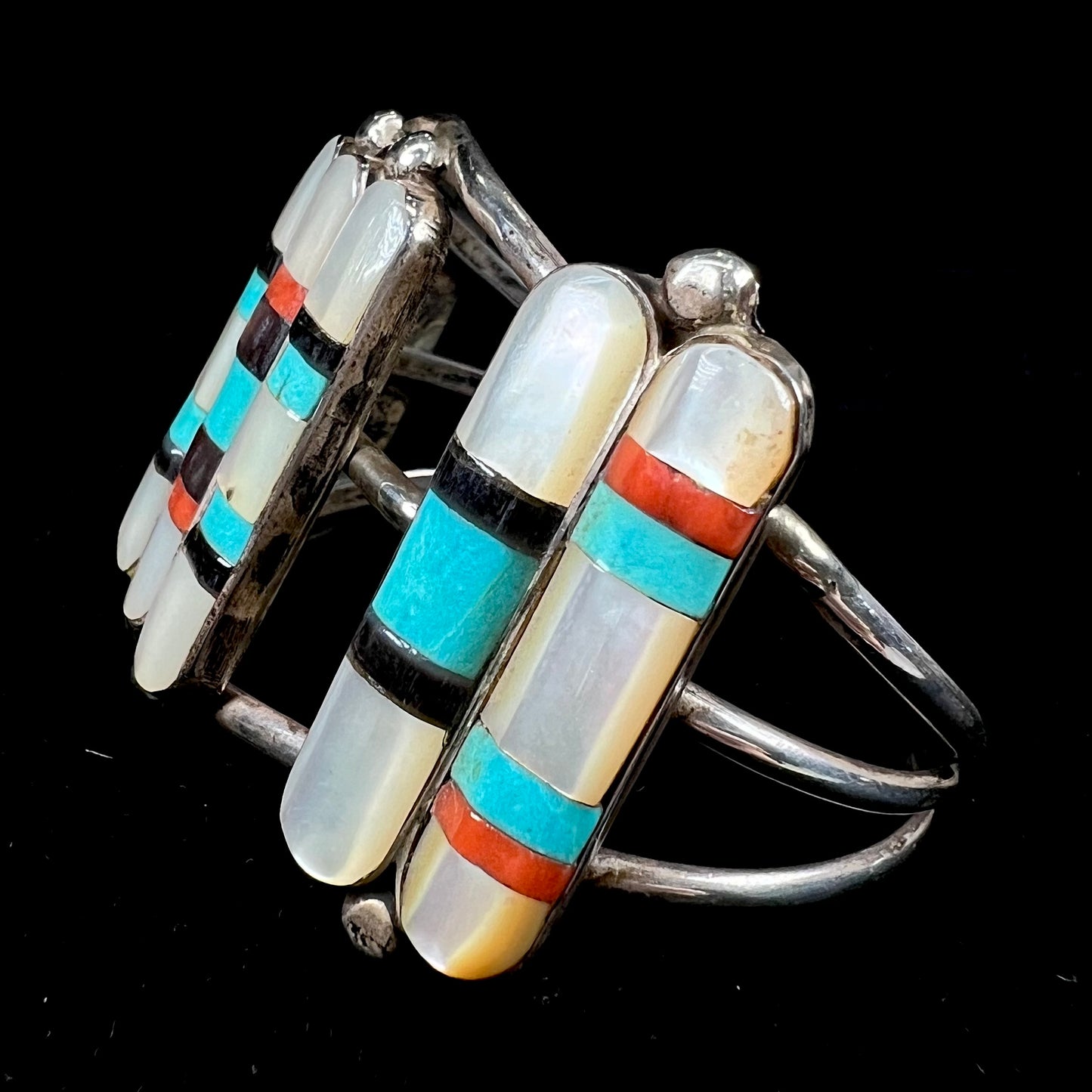 A vintage Zuni Indian-made inlay cuff bracelet set with mother of pearl, coral, turquoise, and jet stones. The piece is signed "PONCHO."