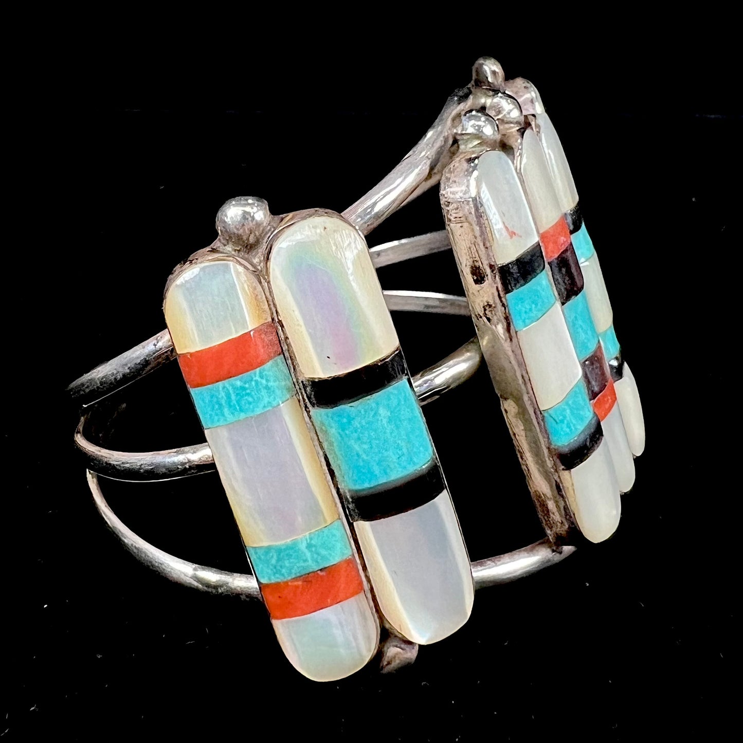 A vintage Zuni Indian-made inlay cuff bracelet set with mother of pearl, coral, turquoise, and jet stones. The piece is signed "PONCHO."