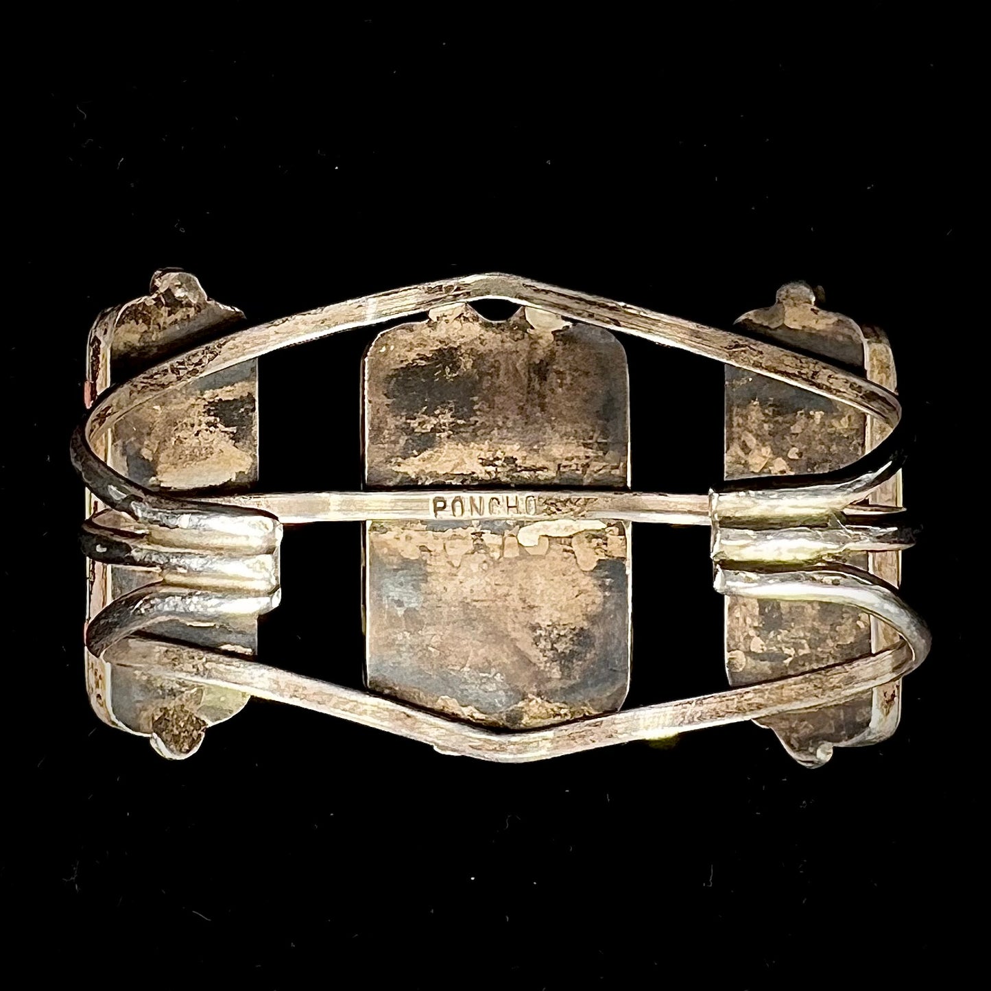 A vintage Zuni Indian-made inlay cuff bracelet set with mother of pearl, coral, turquoise, and jet stones. The piece is signed "PONCHO."