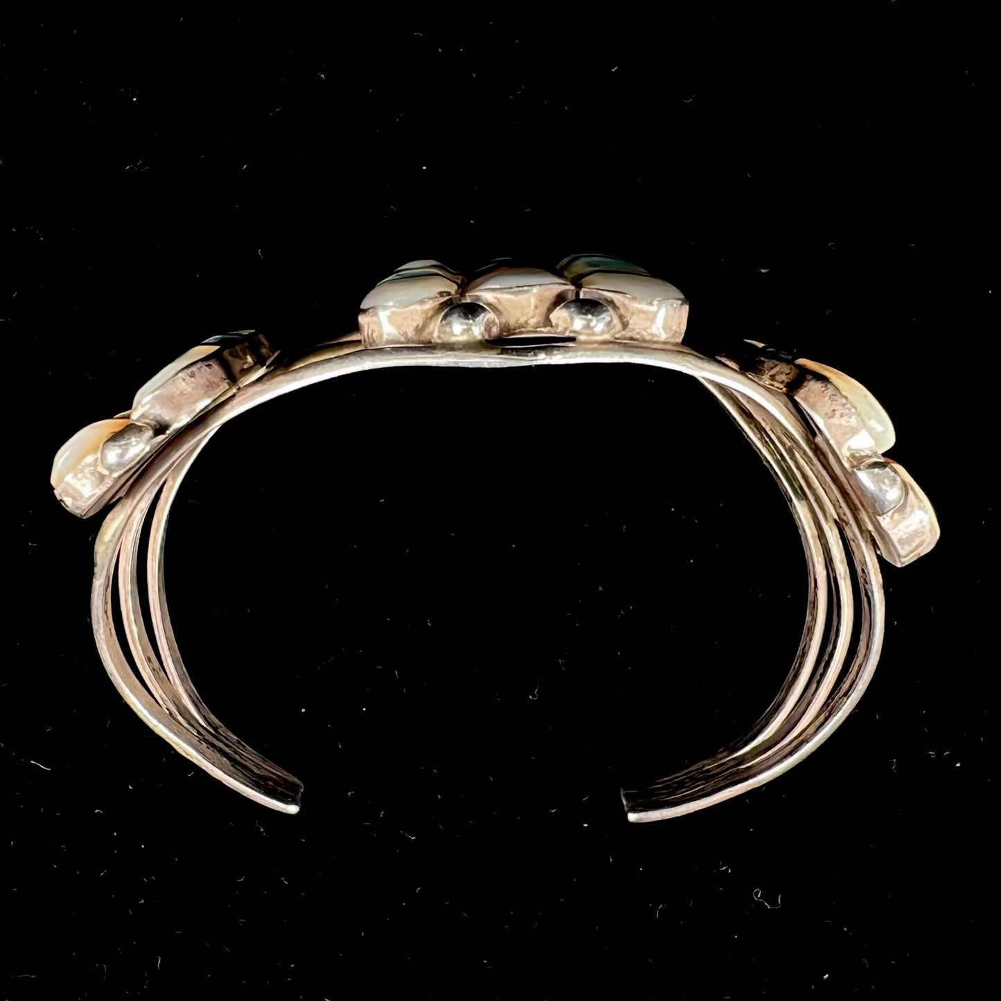 A vintage Zuni Indian-made inlay cuff bracelet set with mother of pearl, coral, turquoise, and jet stones. The piece is signed "PONCHO."