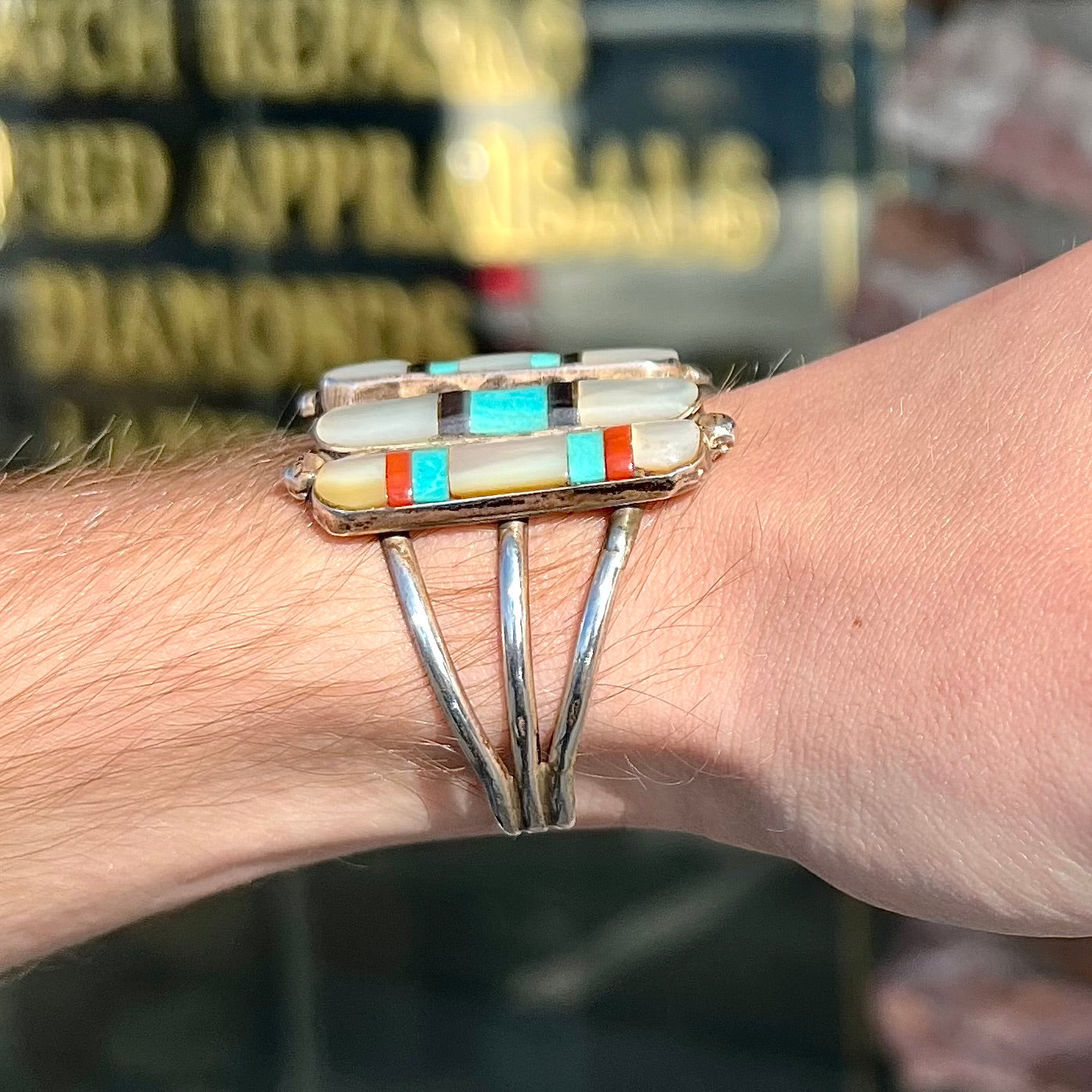 A vintage Zuni Indian-made inlay cuff bracelet set with mother of pearl, coral, turquoise, and jet stones. The piece is signed "PONCHO."