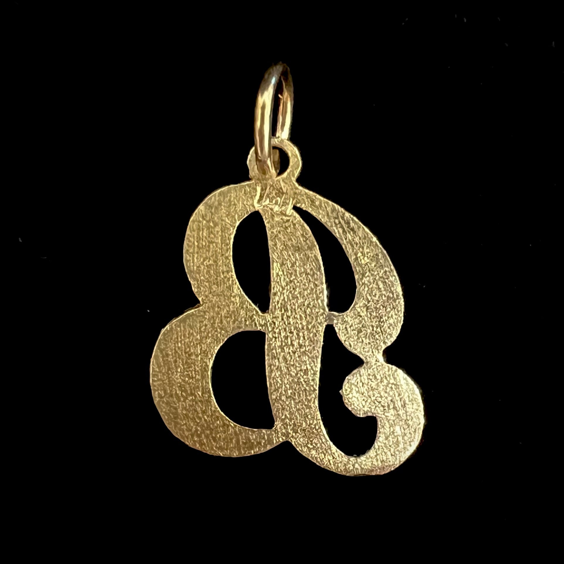 A 14 karat yellow gold stylized script letter "B" pendant, resembling the Barbie logo.