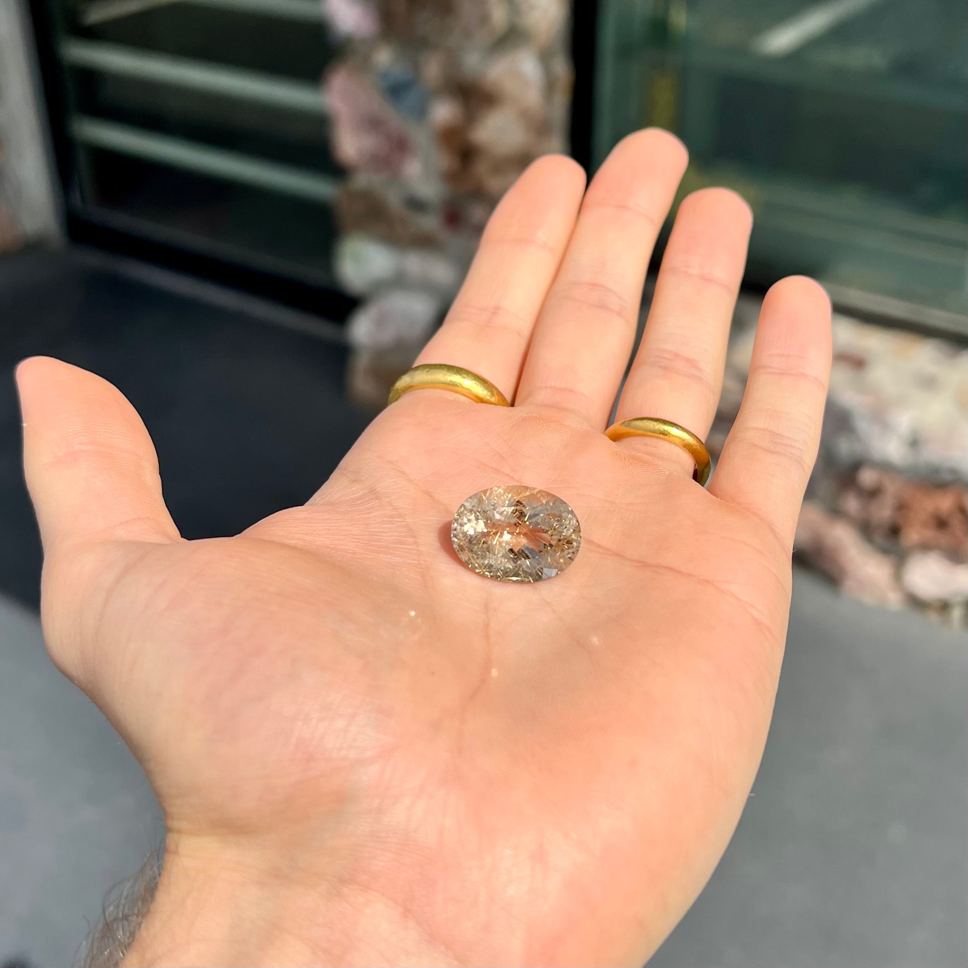 A faceted oval cut rutilated quartz gemstone.  The stone is smoky color with golden rutile needle inclusions.