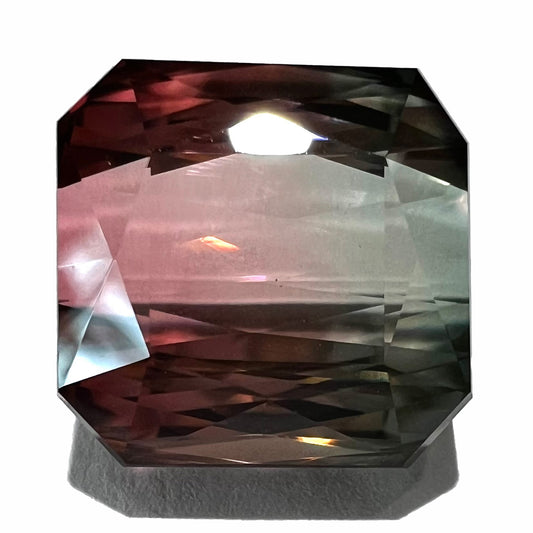 A loose, faceted modified emerald cut bicolor tourmaline gemstone.  The stone transitions from dark pink to dark green colors.