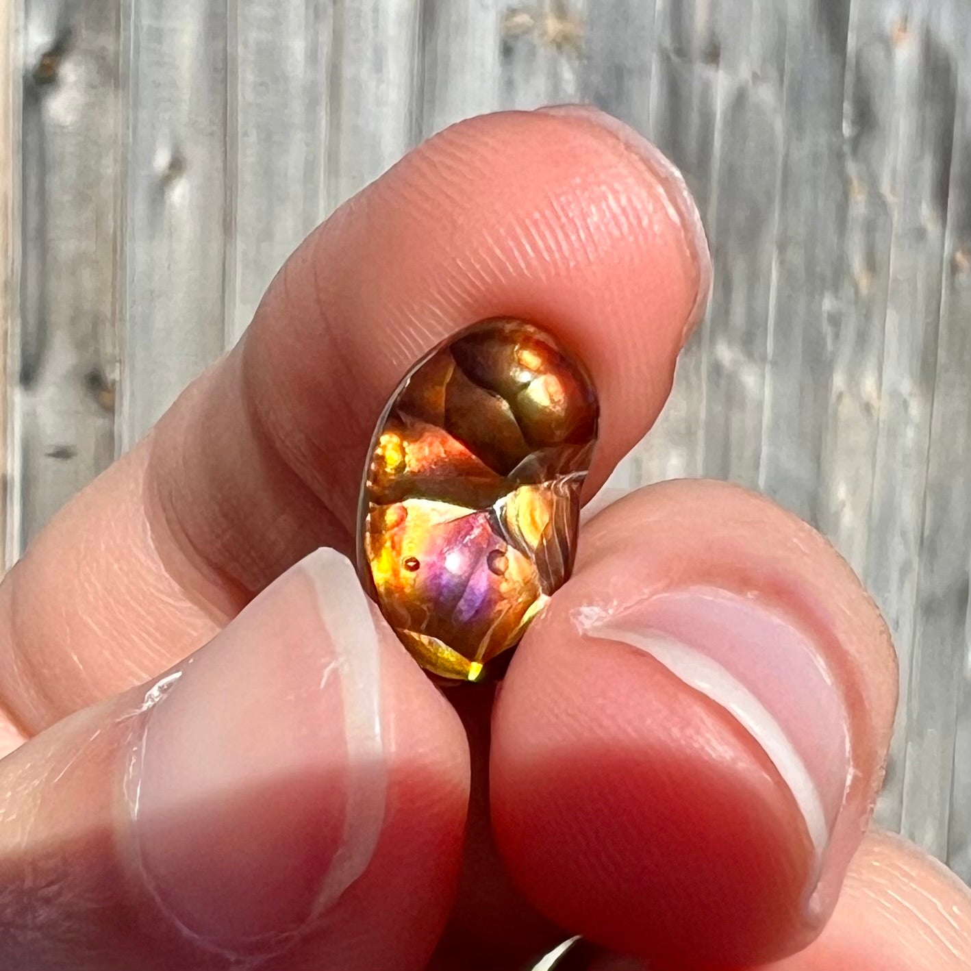 A loose Mexican fire agate gemstone.  The stone is red with a puddle of purple and exhibits a metallic luster.
