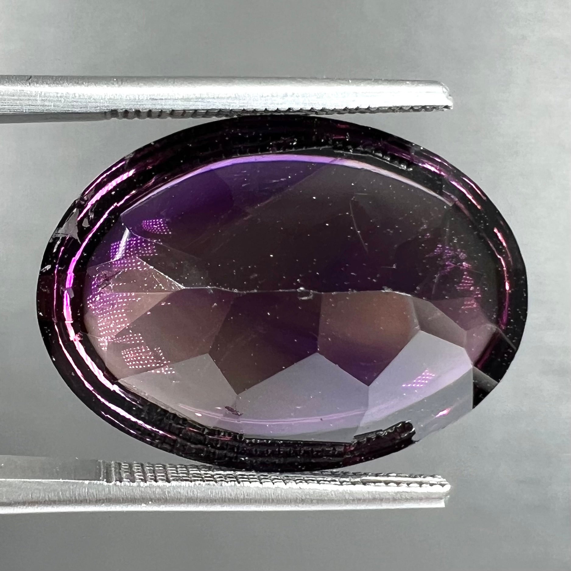 A loose, oval buff top cut amethyst gemstone.  The top of the stone is domed, and the bottom is faceted.