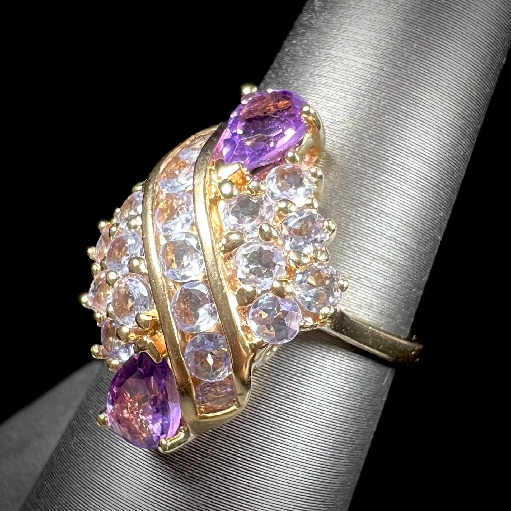 A ladies' gold ring set with a cluster of round tanzanites and two pear shaped amethyst accent stones.