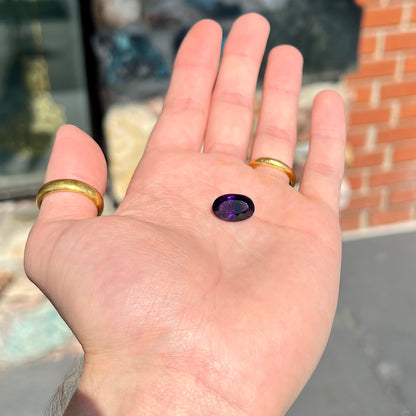 A loose, faceted oval cut Siberian amethyst gemstone.  The stone is purple color with blue and red flashes.