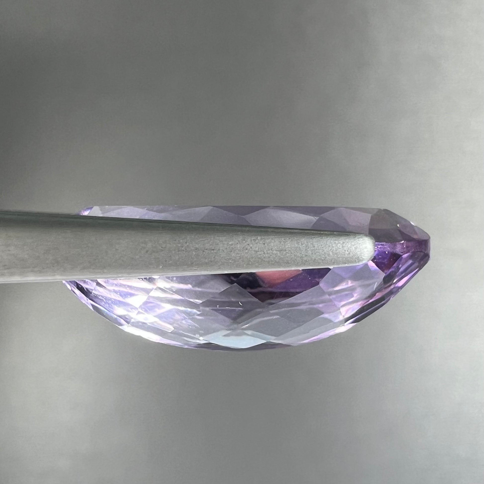 A loose marquise cut amethyst gemstone.  The stone is a light purple color and has scratches along the surface.