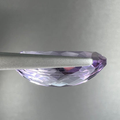 A loose marquise cut amethyst gemstone.  The stone is a light purple color and has scratches along the surface.