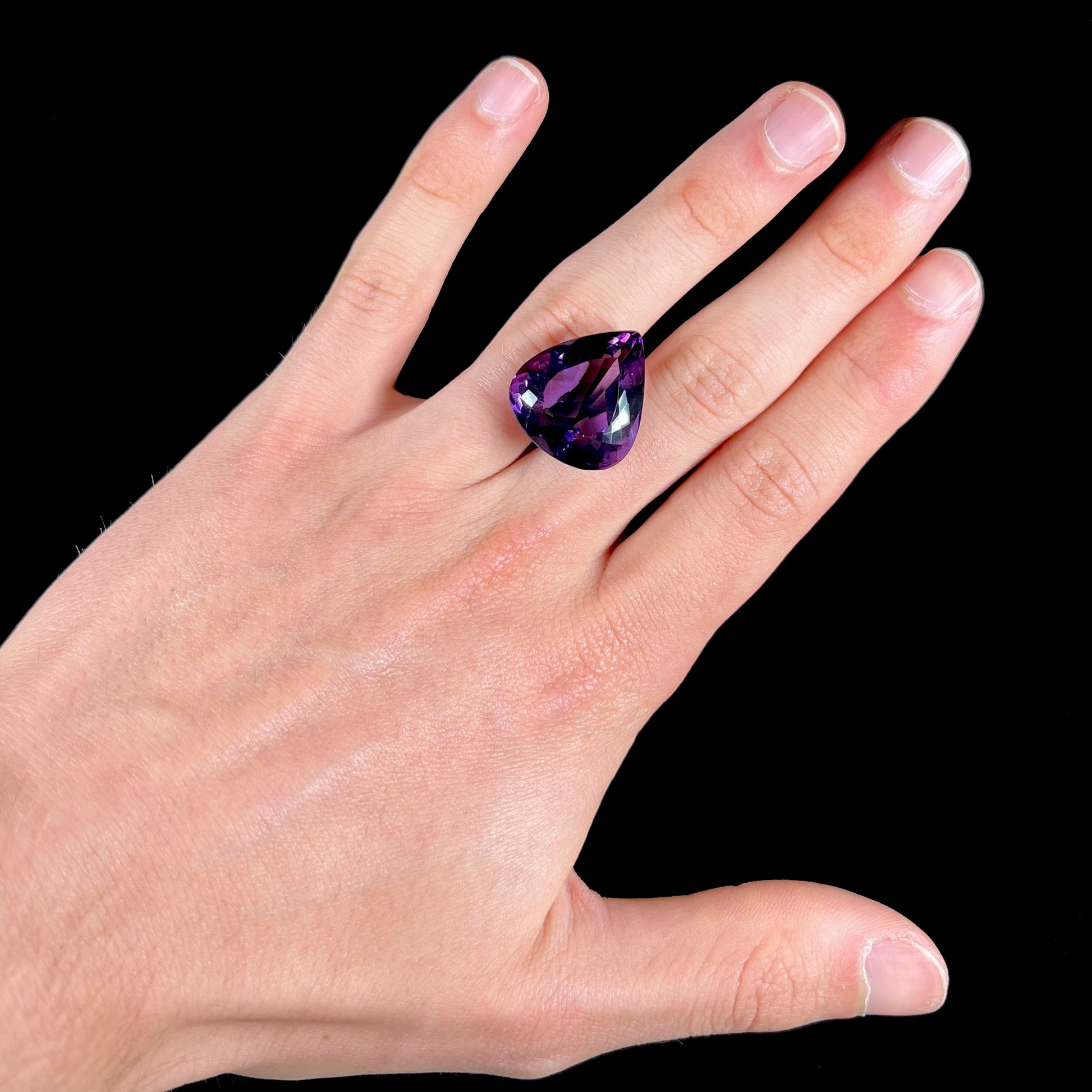 A large, pear shaped amethyst gemstone.  The stone is a dark purple color.